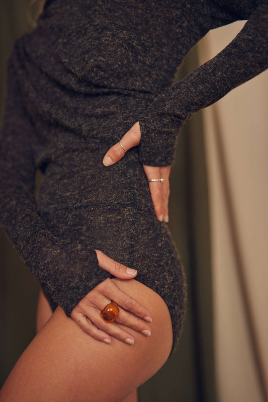 Woman showcasing black recycled jersey drape bodysuit with thumb holes and stylish accessories.
