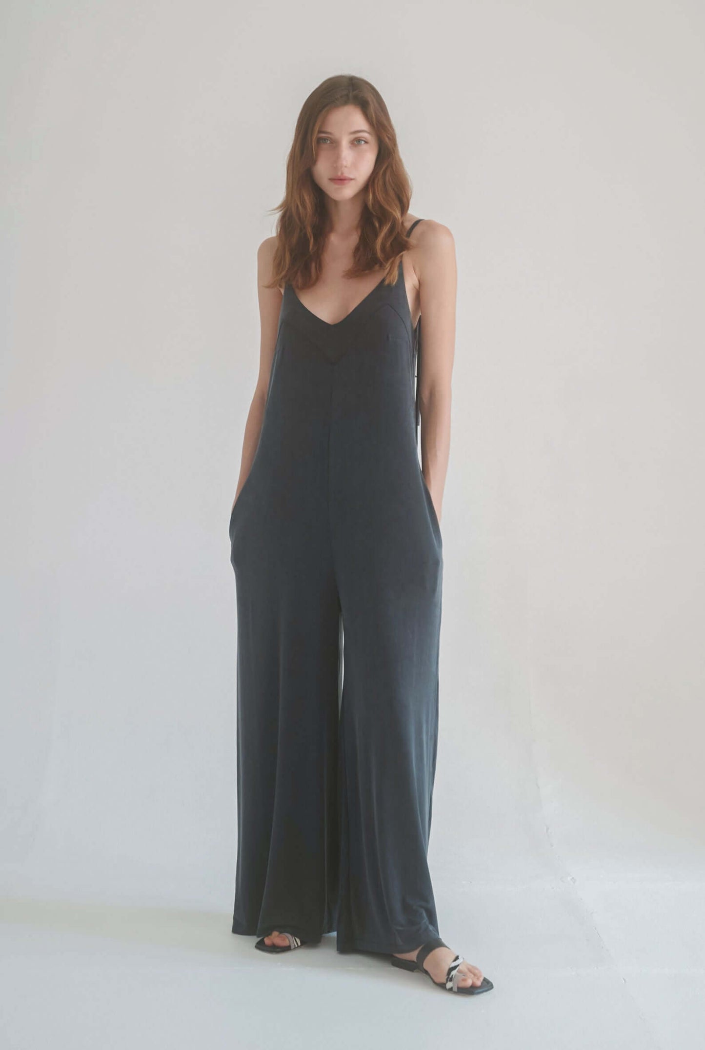 Model wearing a slate black wide jumpsuit with adjustable straps and pockets, showcasing Ecovero viscose fabric.
