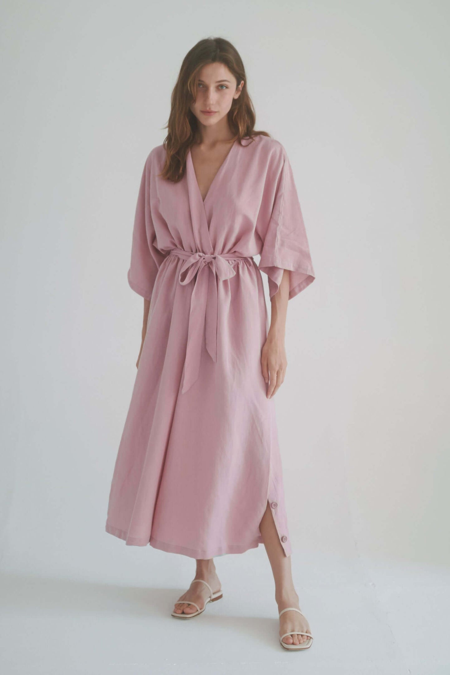 Model wearing a pink kimono-style jumpsuit with a wrap top, belt, and side slits.