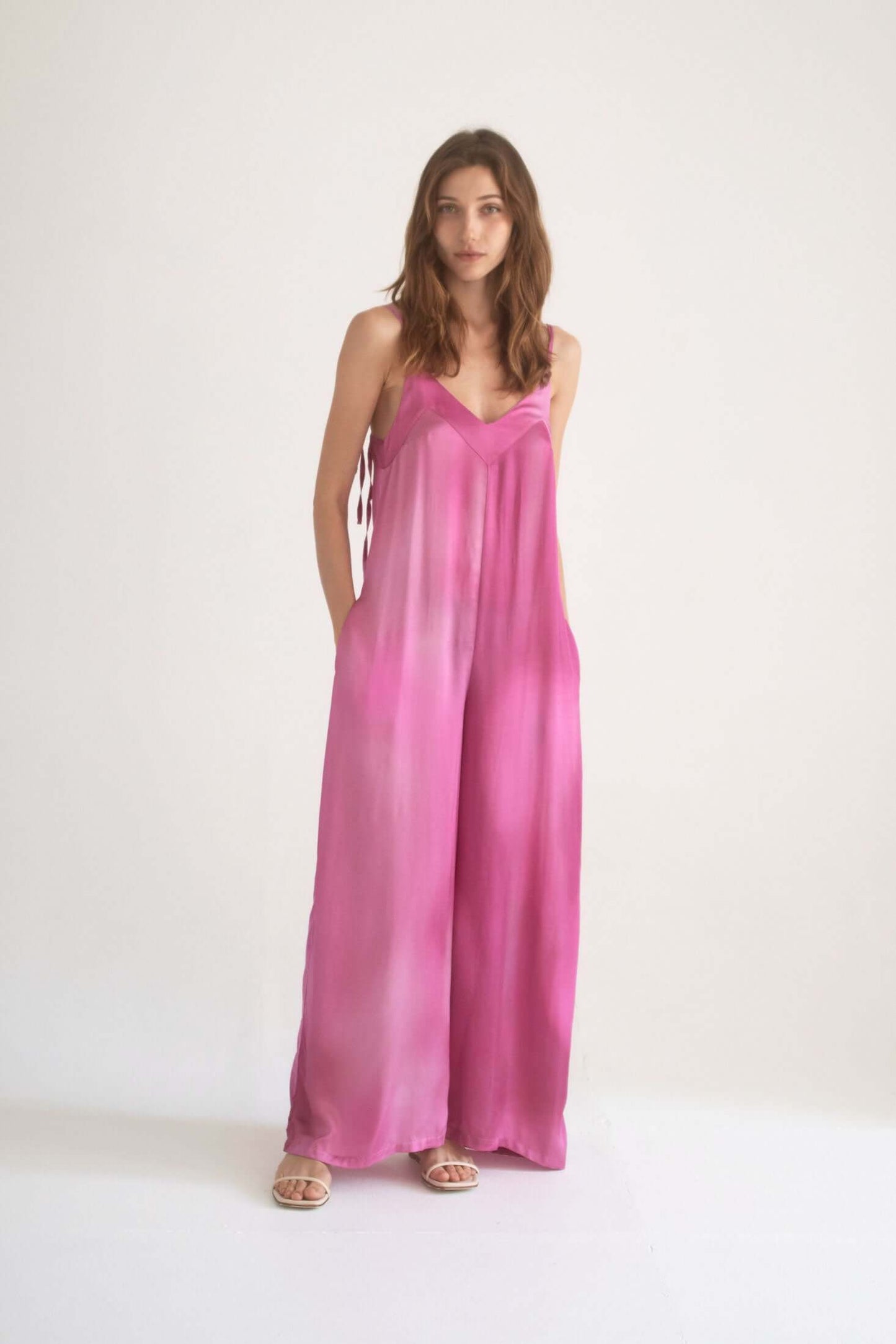 Model wearing a lightweight printed wide jumpsuit in pink, featuring adjustable straps and a flowy silhouette.