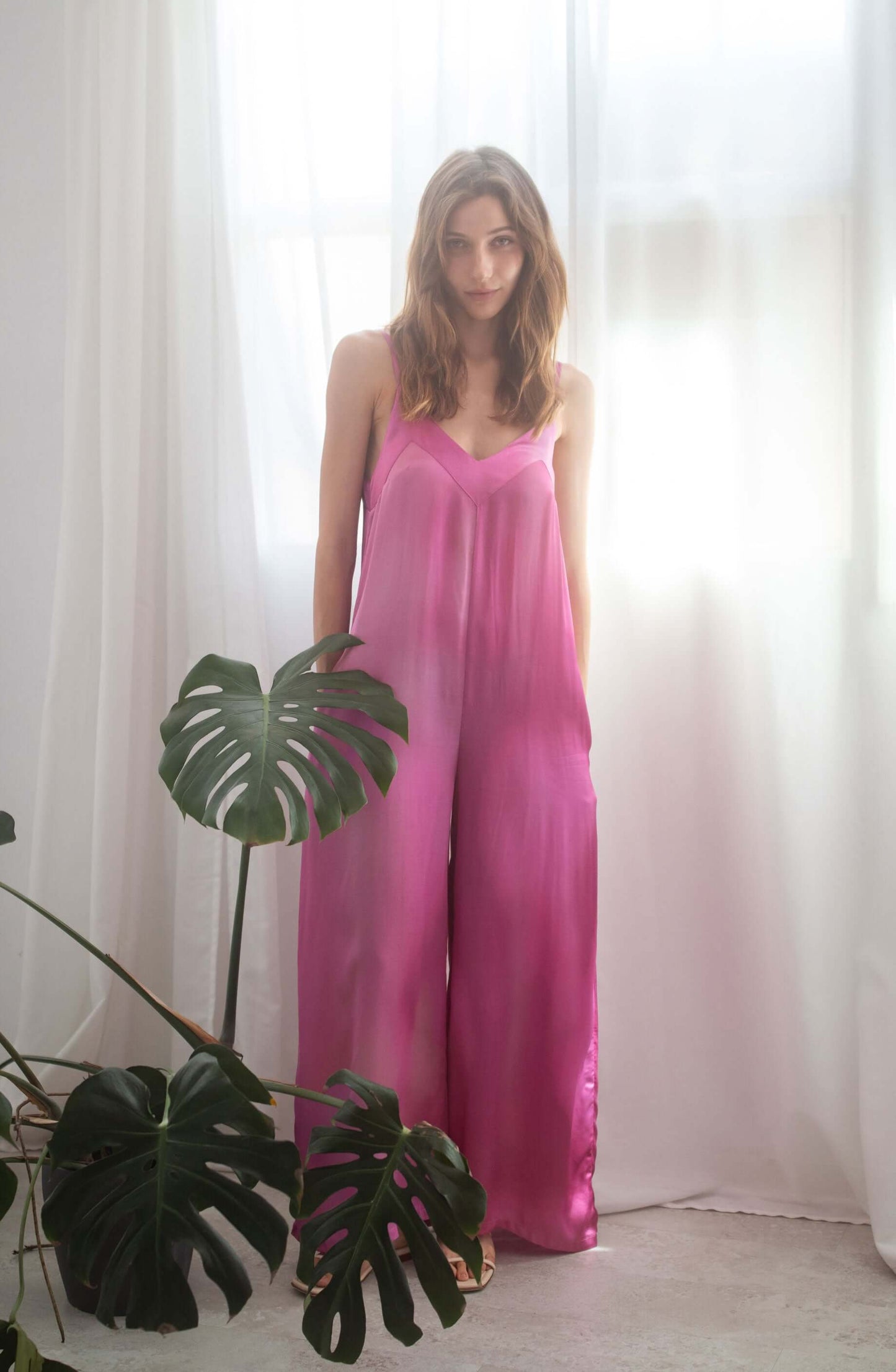 Model wearing a pink printed wide jumpsuit made from 100% Ecovero viscose, showcasing adjustable straps and a lightweight feel.