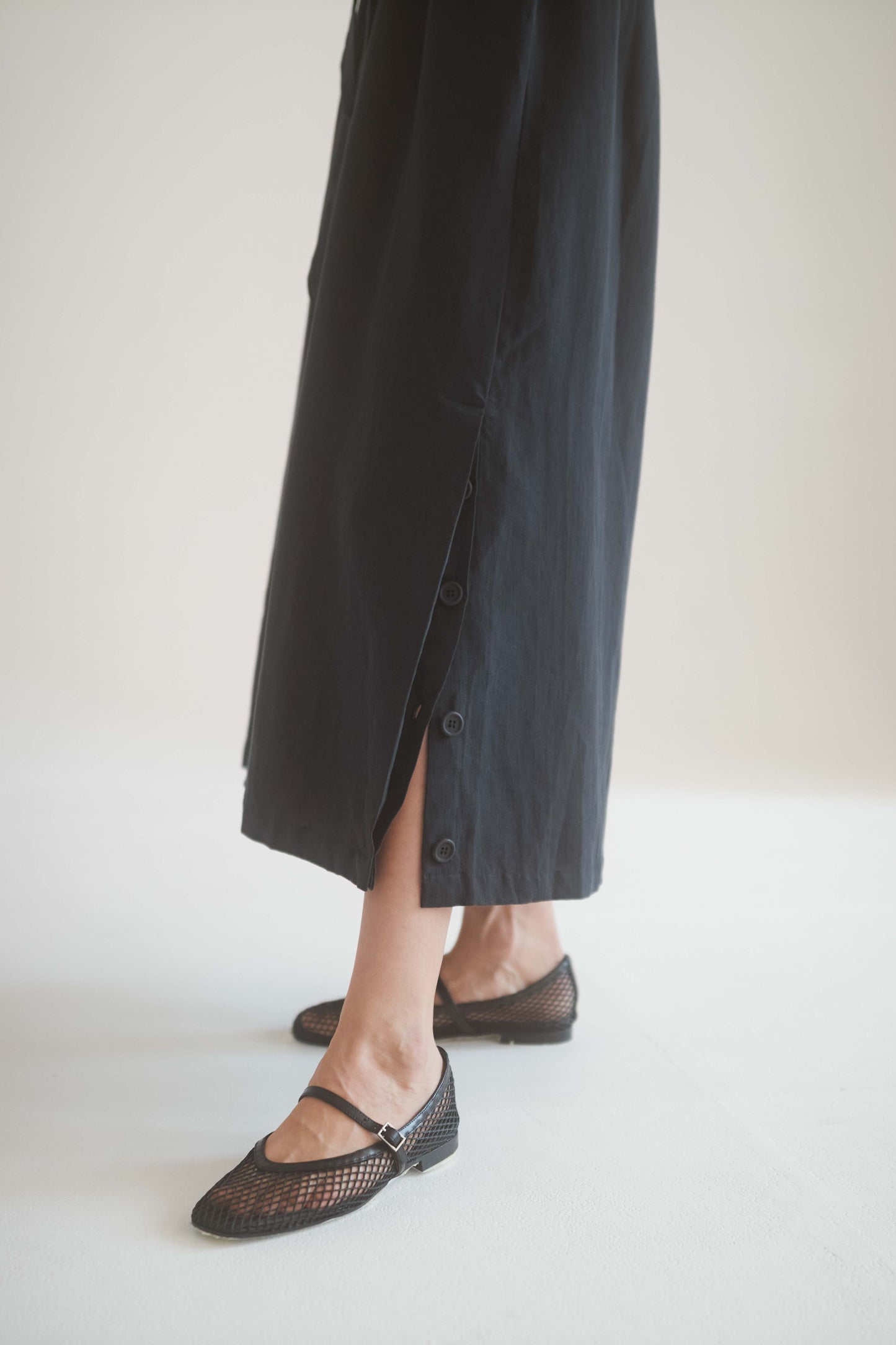 Close-up of a model wearing a black kimono jumpsuit with button details and stylish black shoes.
