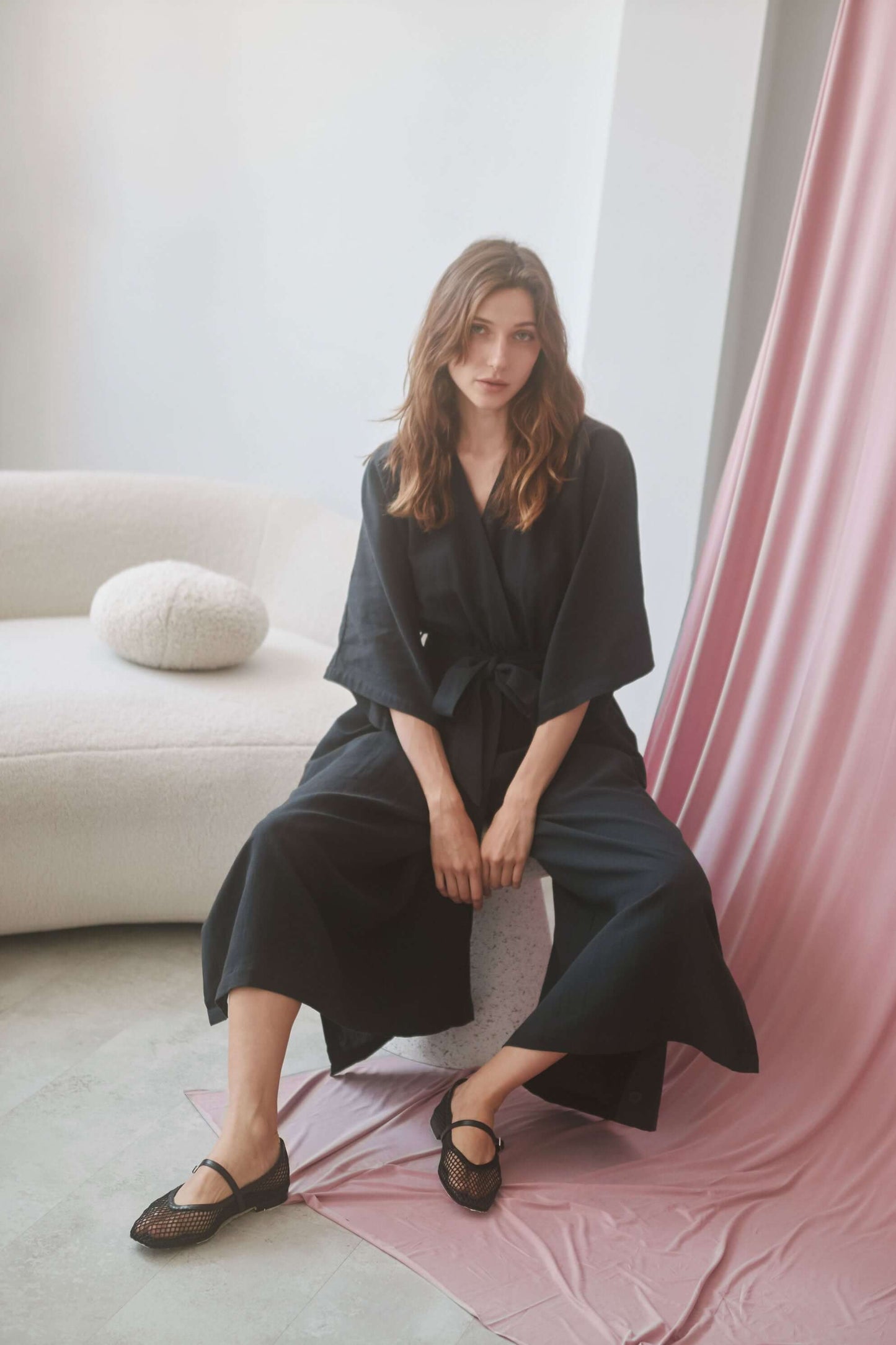 Model wearing a black kimono jumpsuit with a wrap top and belt, showcasing side pockets and stylish design.