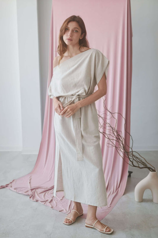Model wearing a natural drape dress with off-shoulder neckline and elasticated waist, styled against a pink backdrop.