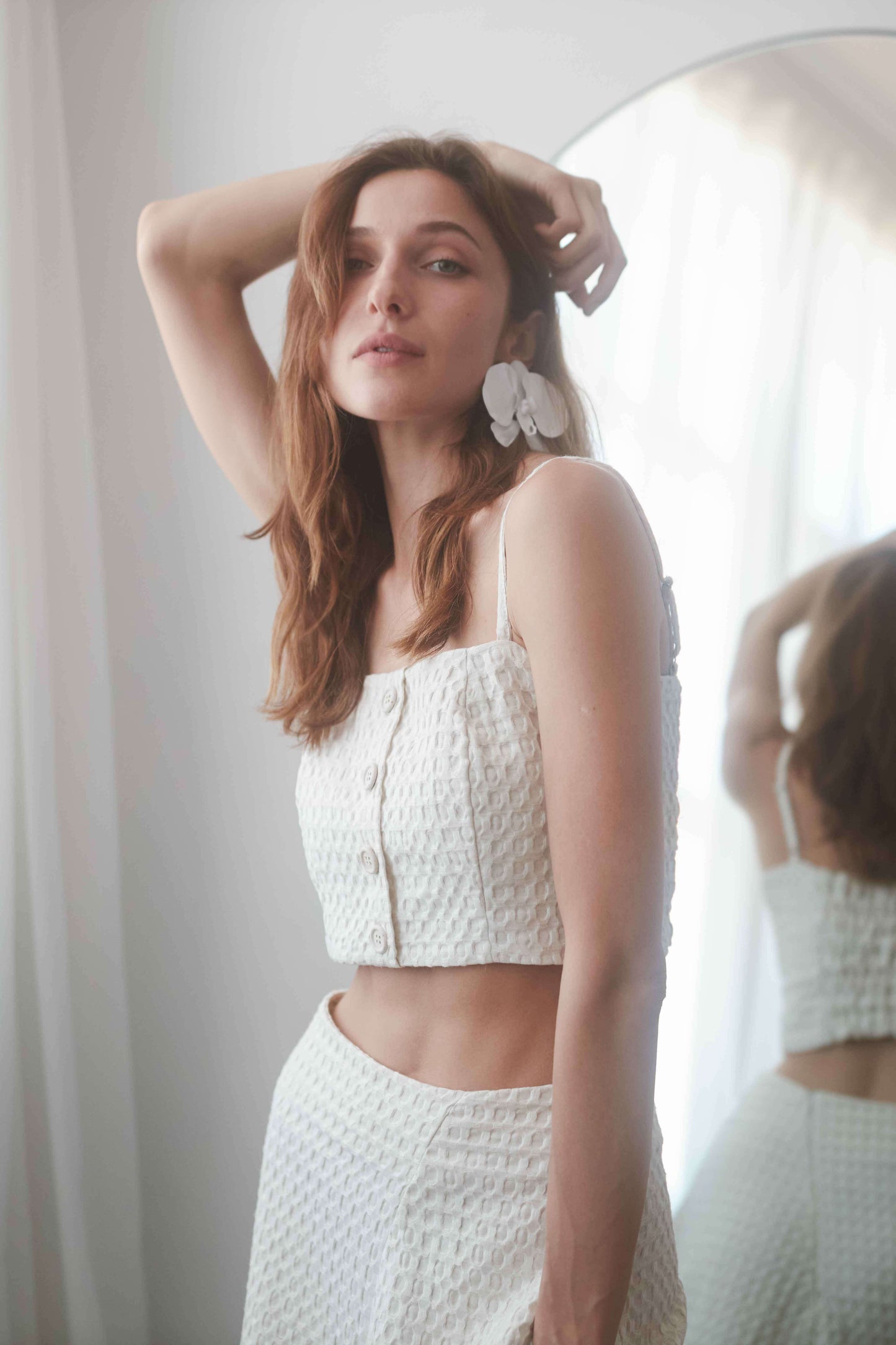Model wearing an ecru waffle crop top with adjustable straps, showcasing a stylish layered look in natural light.