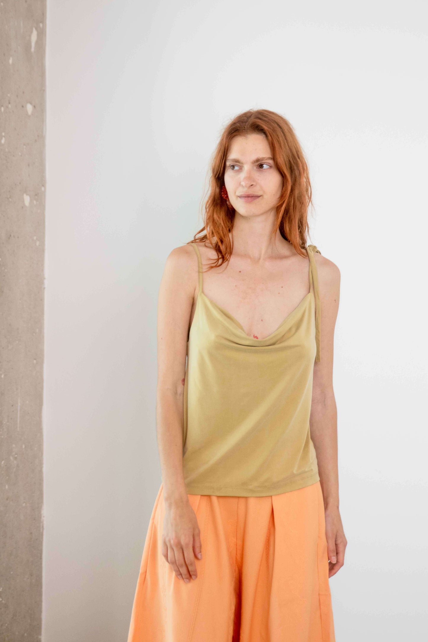 Model wearing a Cupro Drape Slip Top in soft olive, showcasing its flattering draped neckline and adjustable straps.