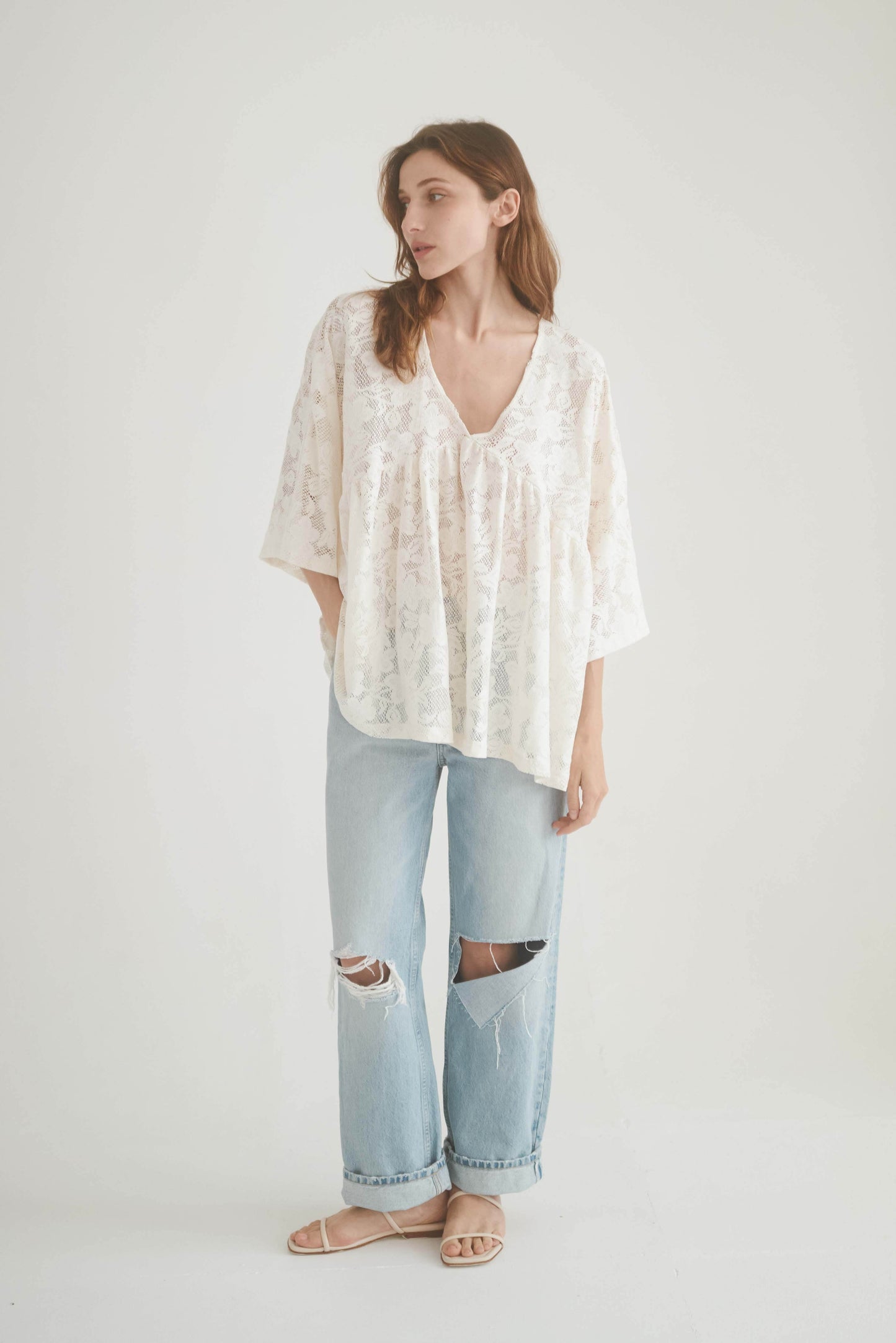 Model wearing a lace boho tunic top with a V-neckline and wide sleeves, paired with ripped jeans.