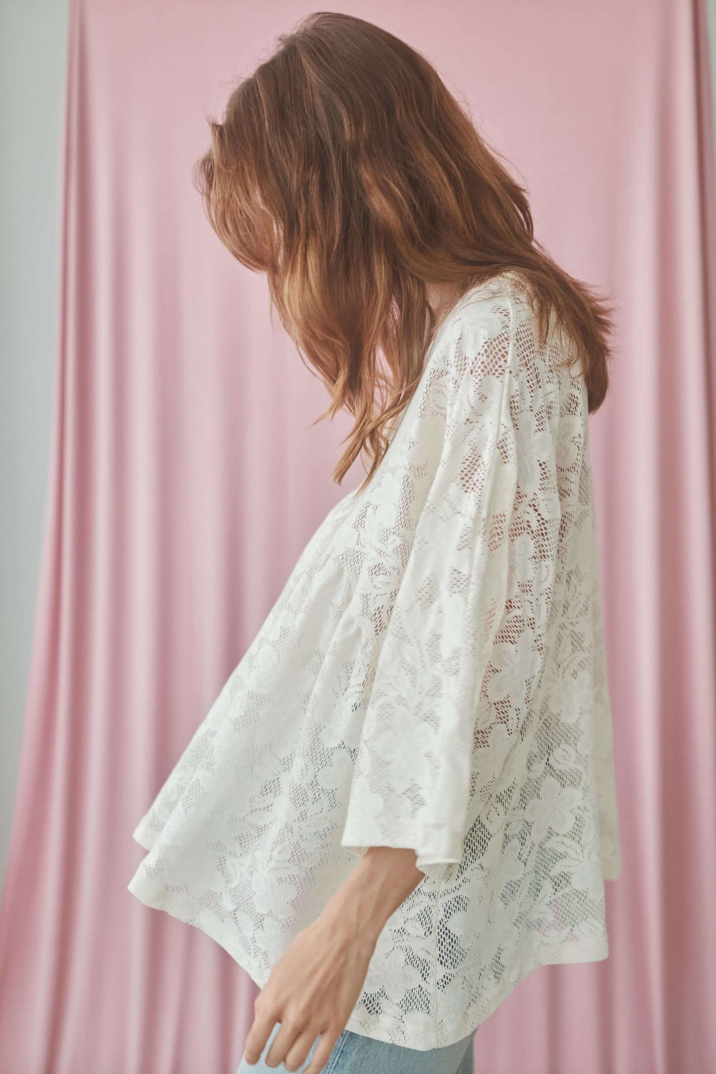 Model wearing a lace boho tunic top with V-neckline and wide sleeves, set against a pink backdrop.