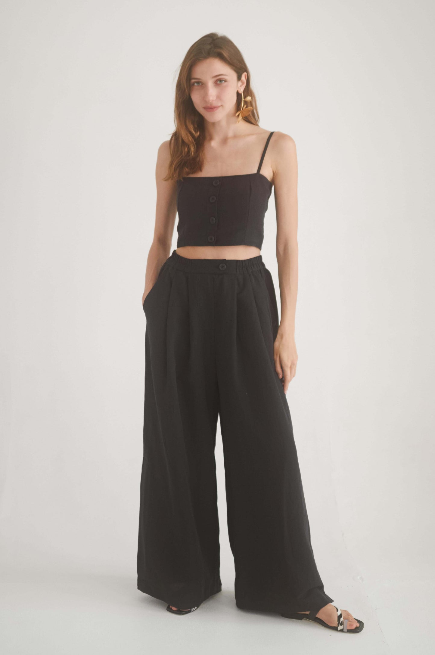 Model wearing a black crop top with adjustable straps and wide black trousers, showcasing a chic and sustainable look.