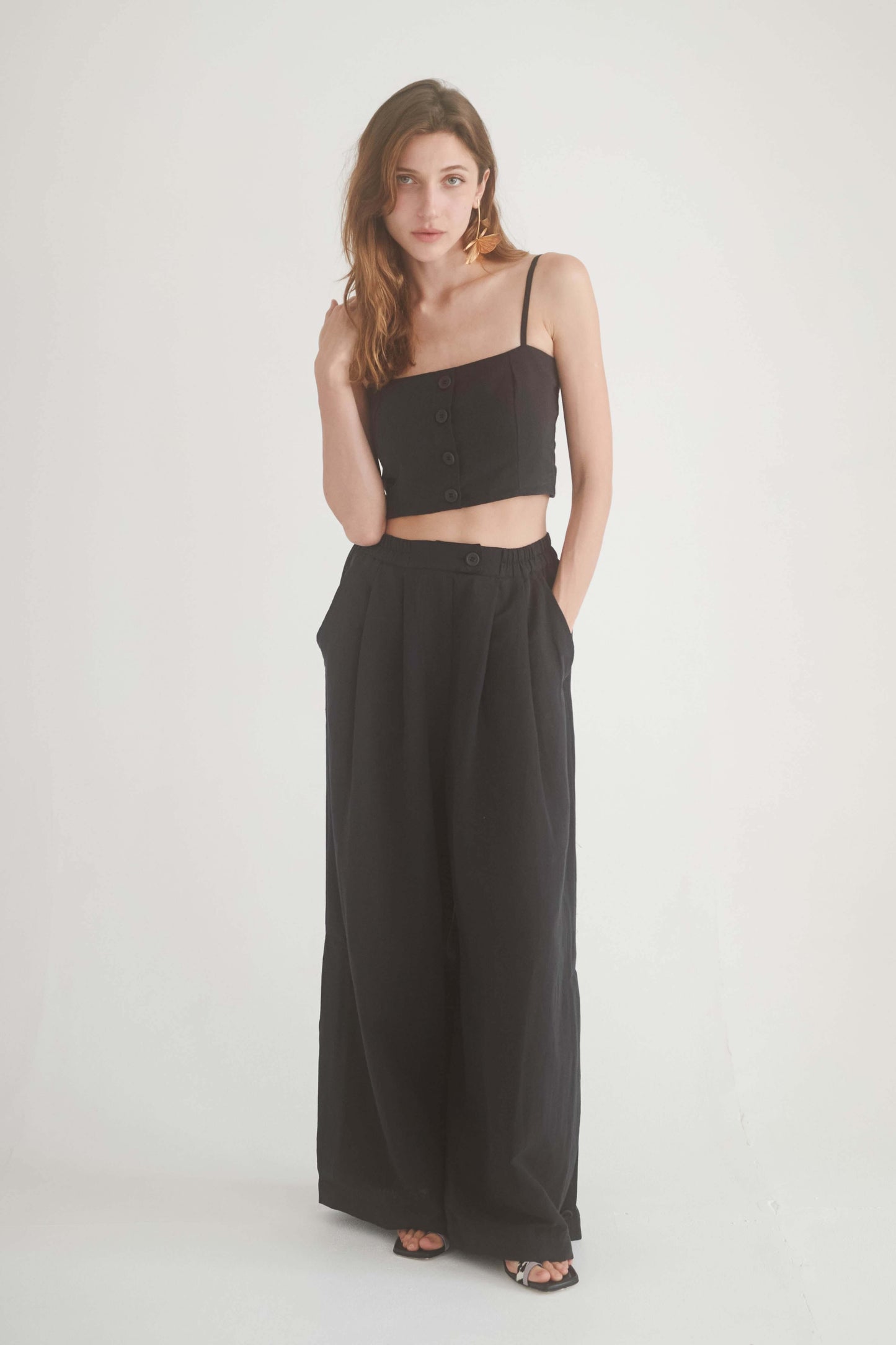 Model showcasing black wide trousers with high waist and elasticated fit, paired with a black crop top.
