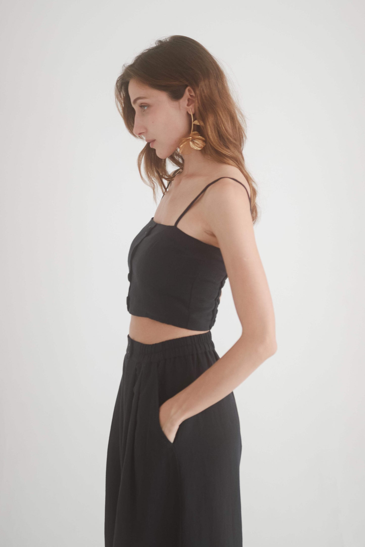 Side view of a model wearing a black crop top with adjustable straps and wide trousers, showcasing eco-friendly fashion.
