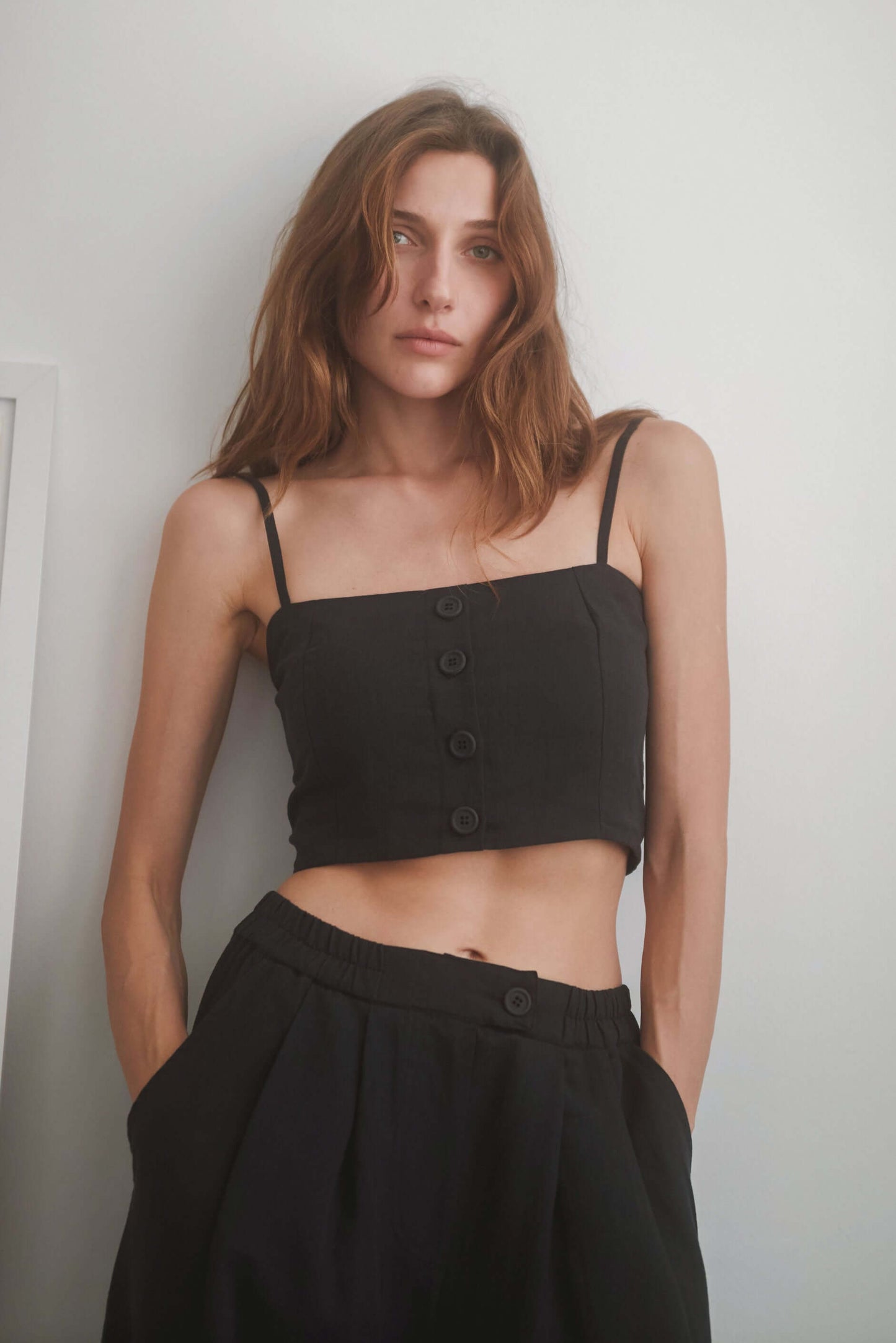 Black crop top with eco-friendly woven fabric, adjustable straps, and eco buttons, styled with matching wide trousers.