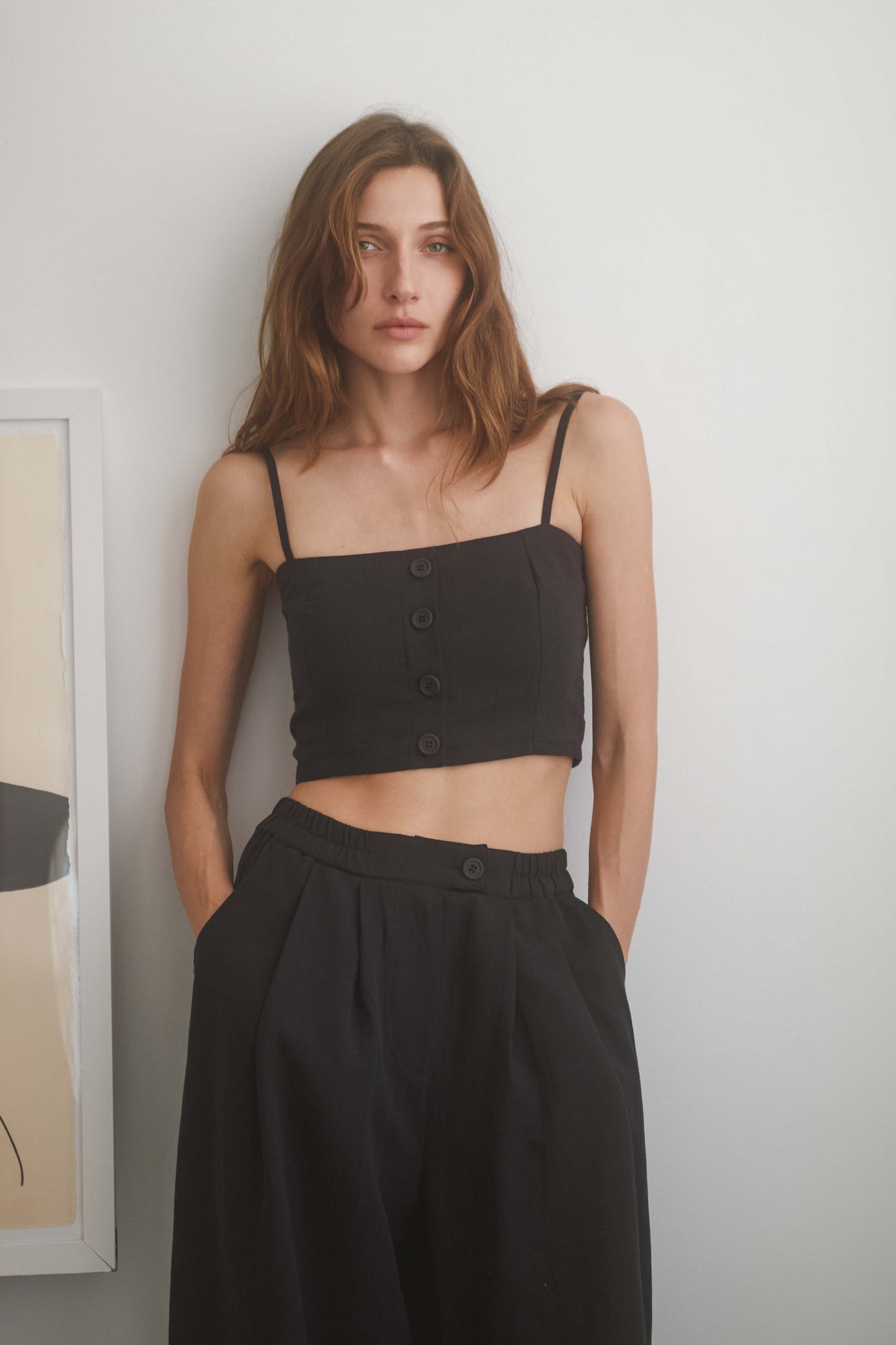 Model wearing a black crop top with eco buttons and adjustable straps, paired with wide trousers.