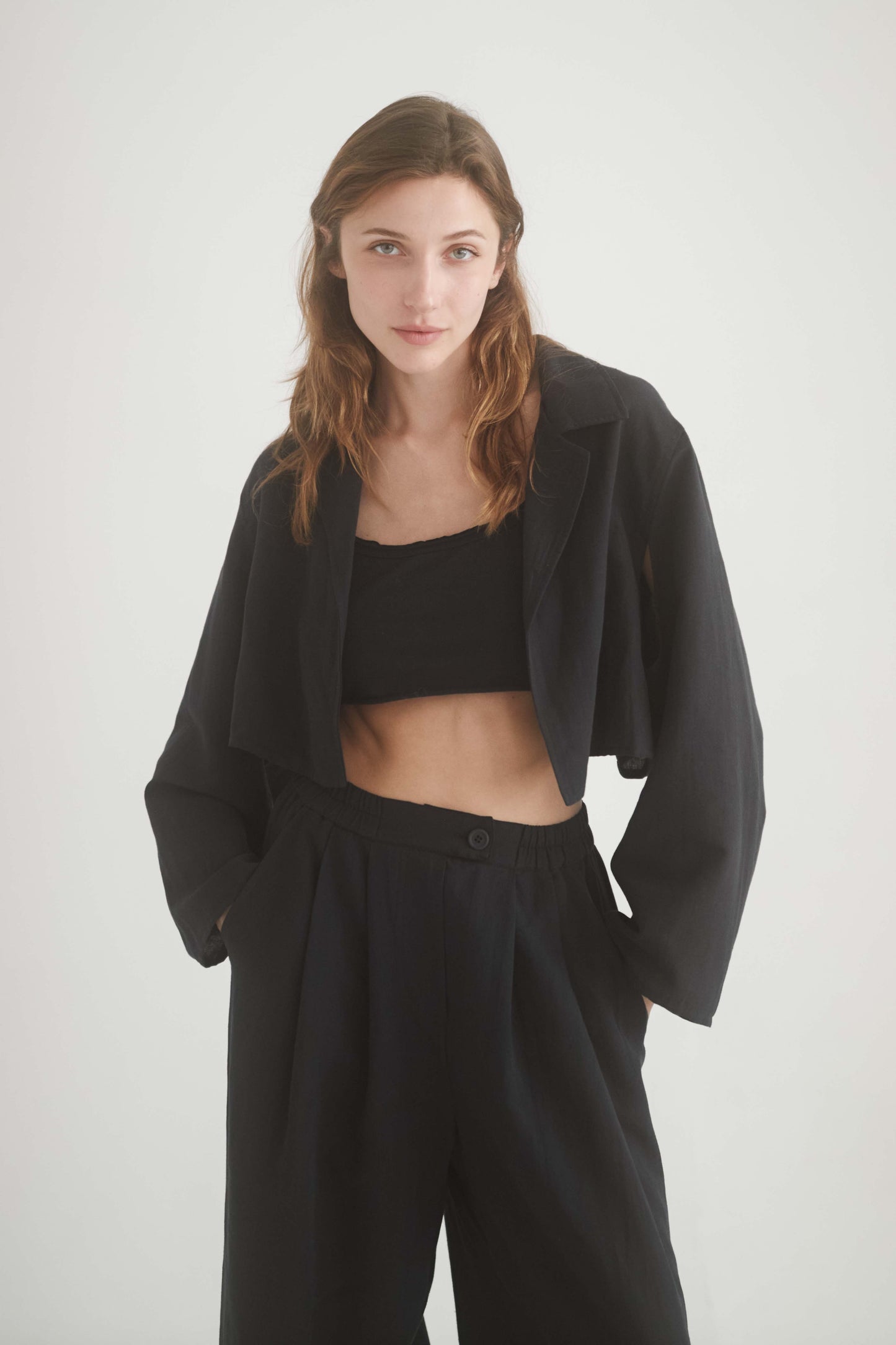 Model wearing a black crop jacket with armhole cutouts and wide trousers, showcasing a stylish and sustainable outfit.