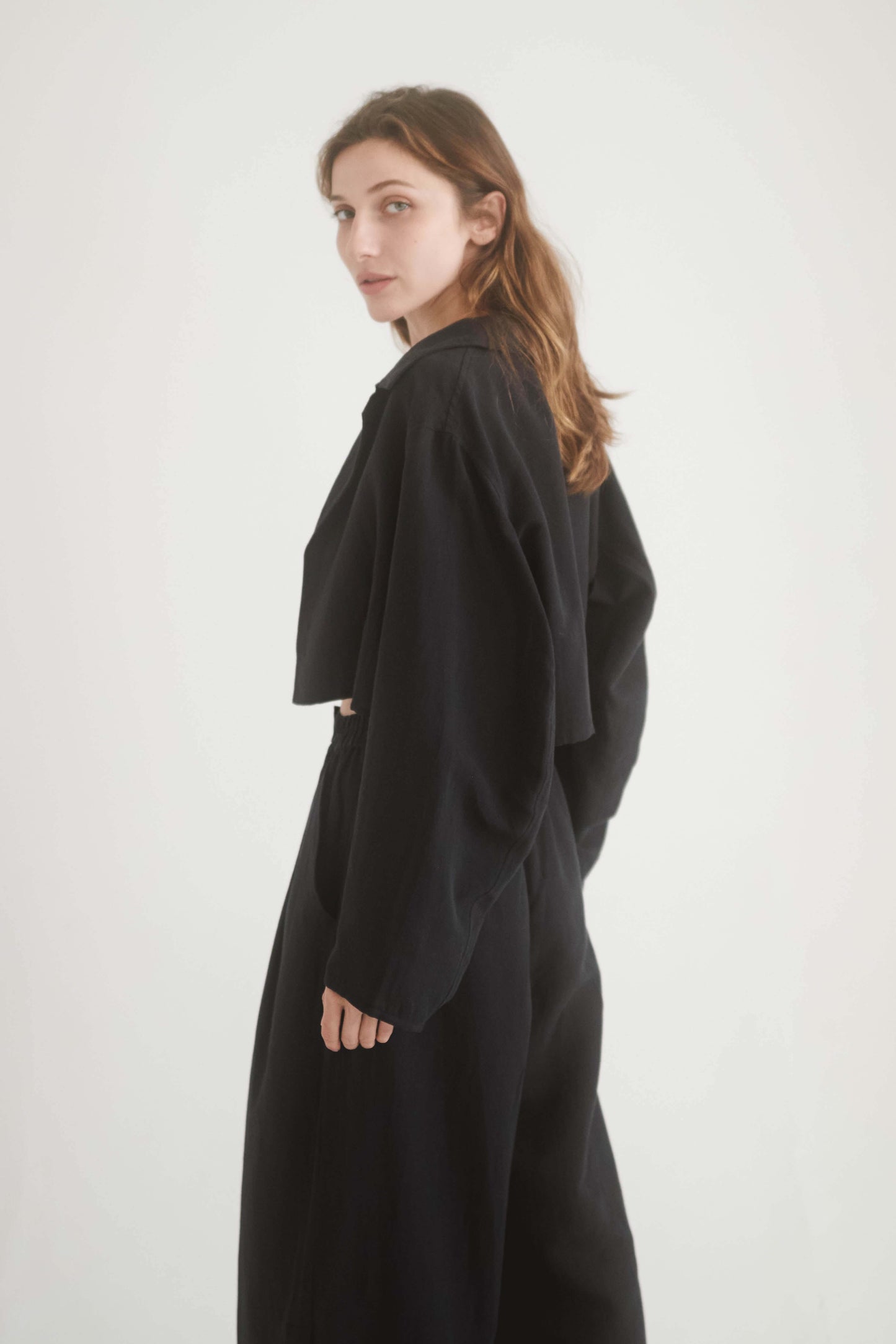 Woman wearing a stylish black cropped jacket made from premium woven fabric, featuring armhole cutouts.