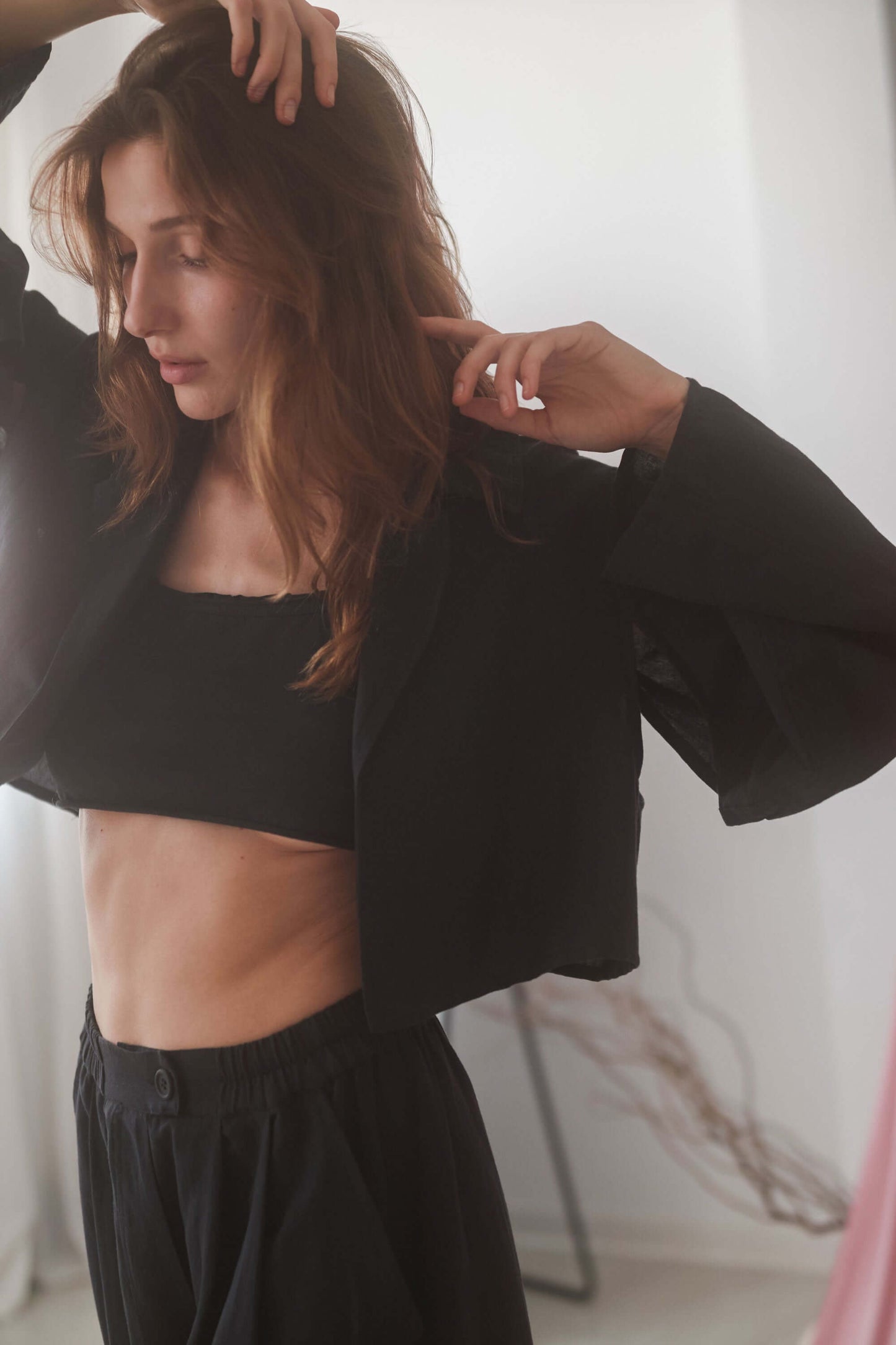 Woman wearing a black cropped jacket with armhole cutouts, styled with wide trousers, showcasing a modern and chic look.
