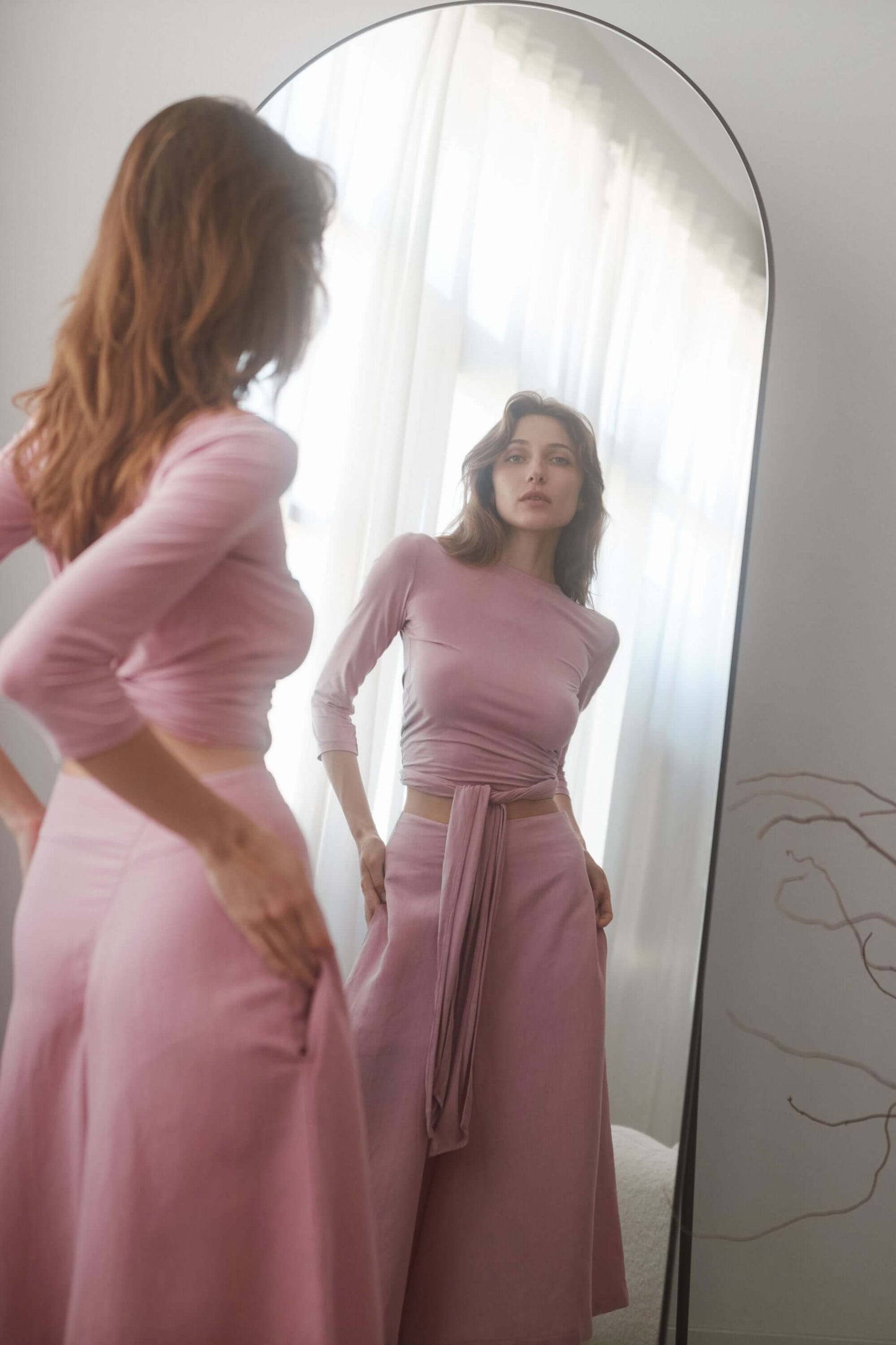 Model wearing rose skirt culottes with a fitted top, showcasing elegant style and sustainable fashion in a mirror.