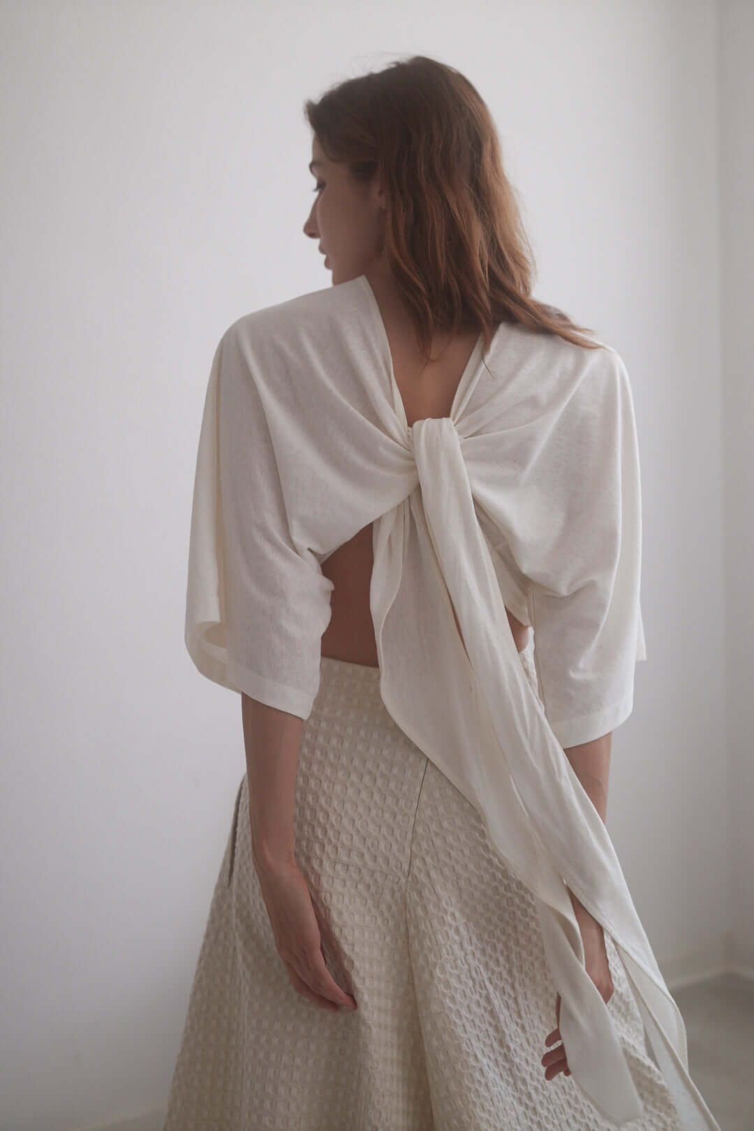 Woman wearing an ecru wrap top with adjustable ties and kimono sleeves, showcasing a back view.