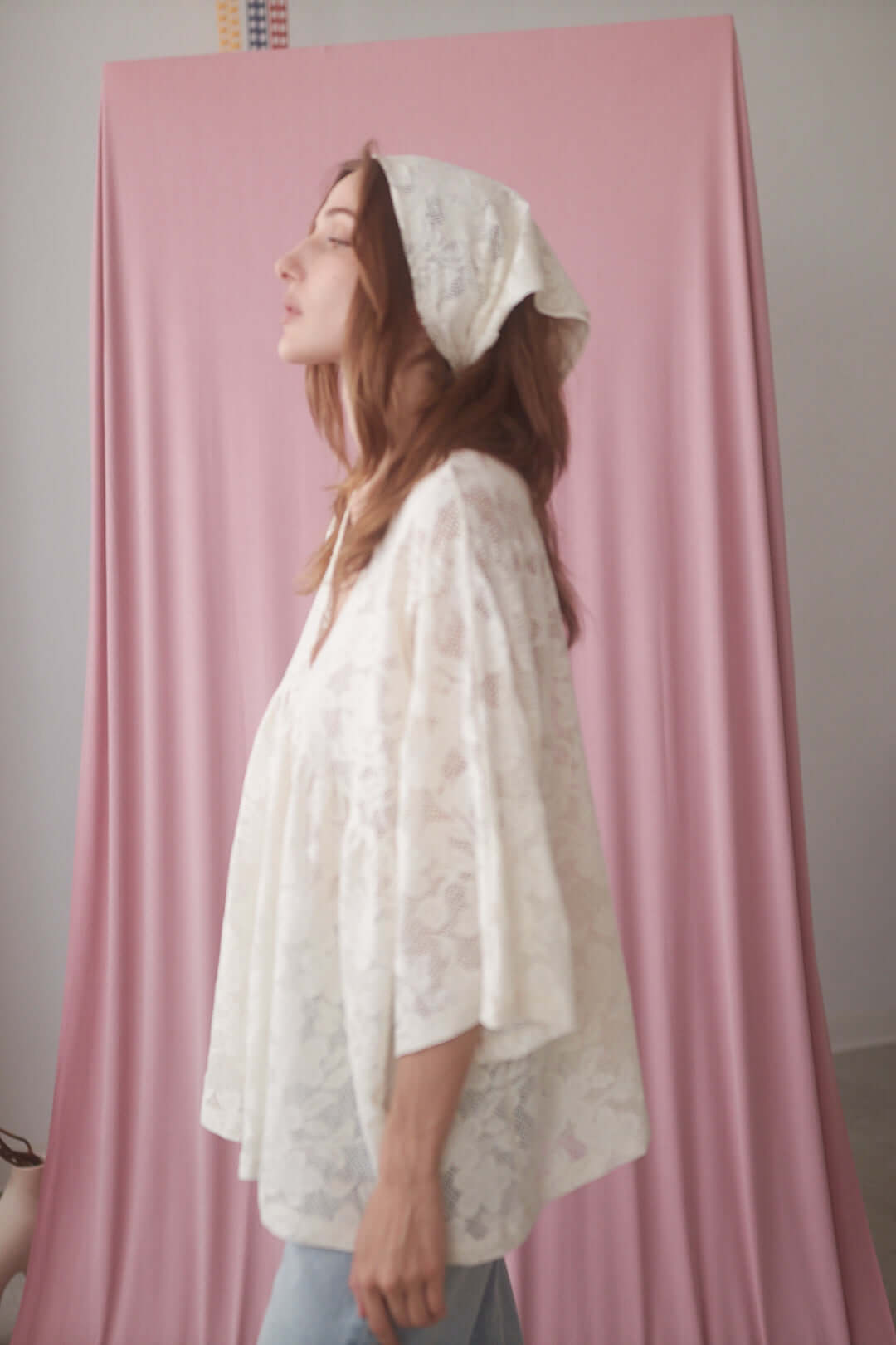 Woman in an ecru small lace scarf, highlighting its delicate knit design against a pink background.