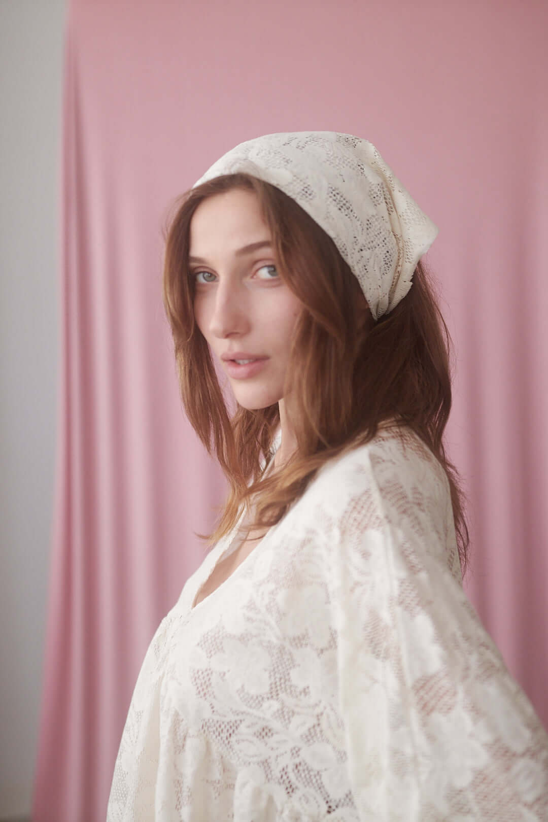 Model wearing a small lace scarf made of organic cotton against a soft pink background, showcasing its delicate style.