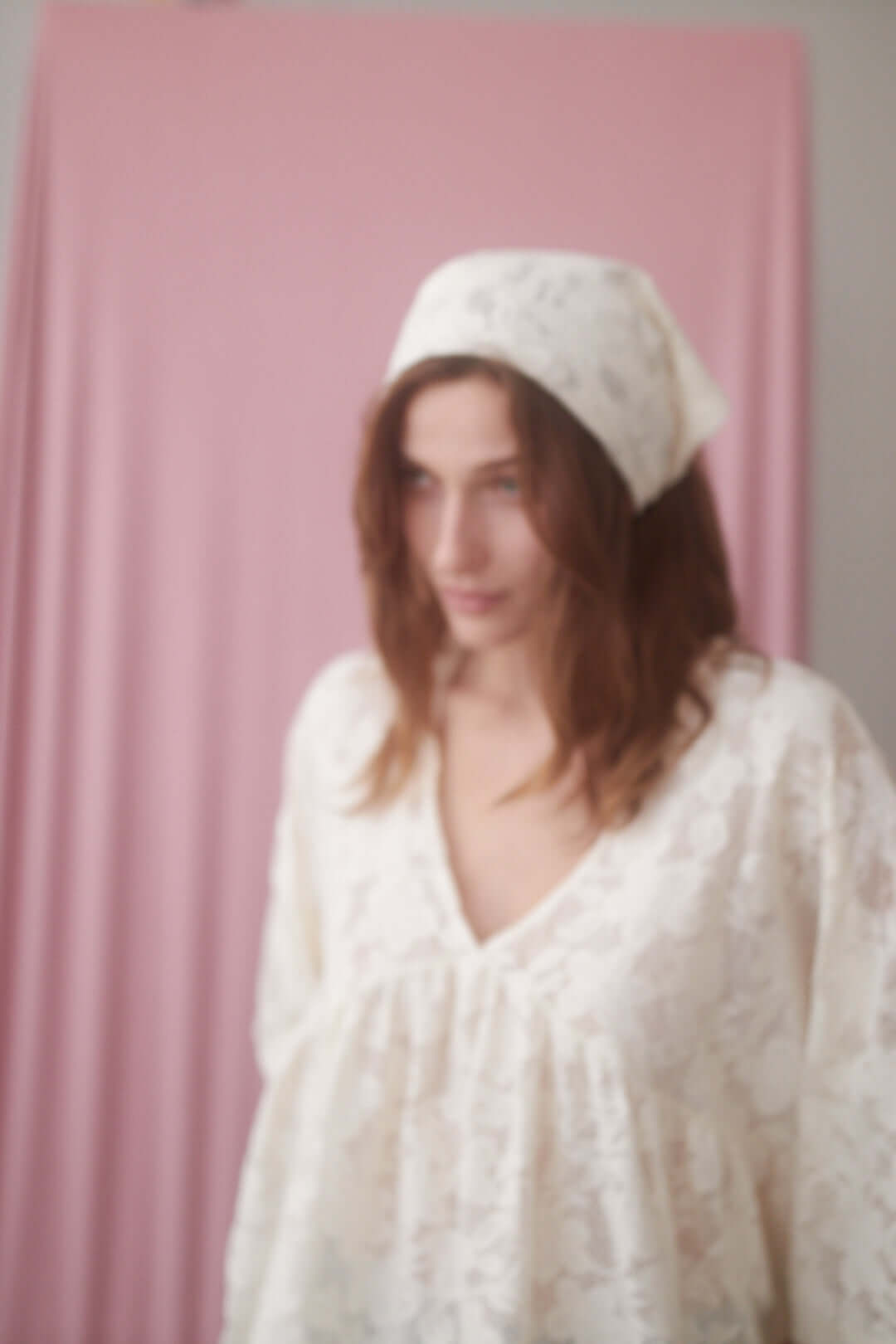 Model wearing a small lace scarf in ecru, showcasing the delicate knitted lace design against a pink backdrop.