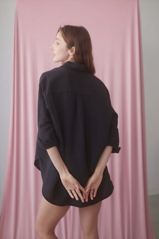 Model wearing a black wide shirt, showcasing its relaxed fit against a soft pink backdrop.
