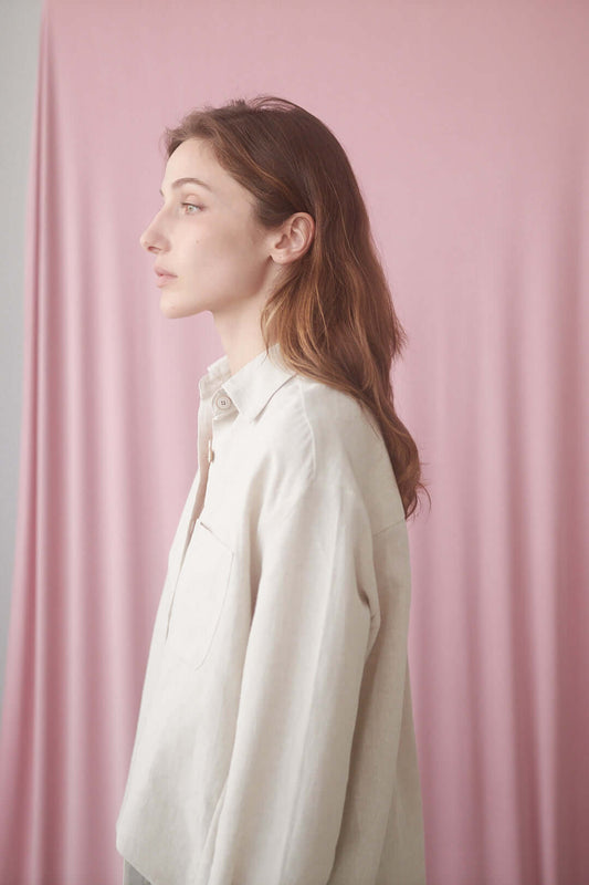 Model wearing a natural wide shirt against a pink background, showcasing its modern fit and eco-friendly design.