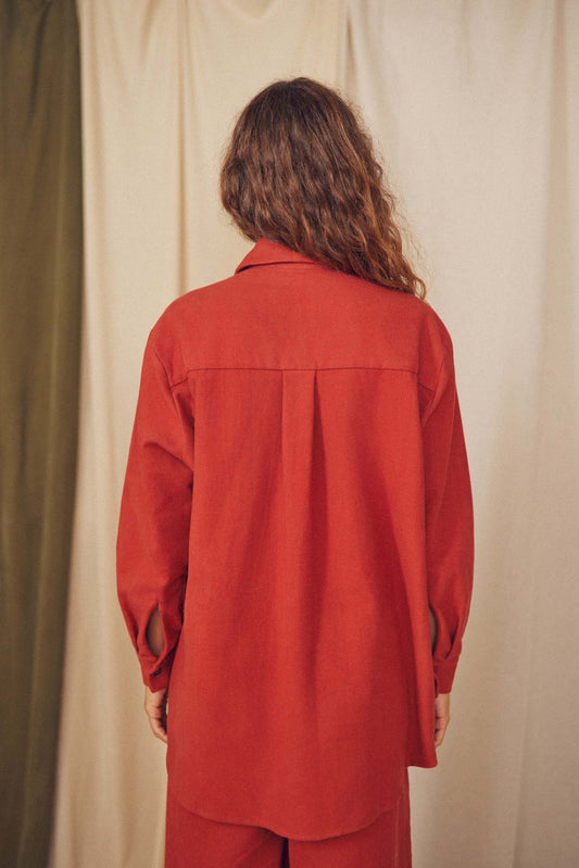 Back view of a model wearing a rust organic cotton wide overshirt, showcasing its oversized silhouette and eco-friendly design.