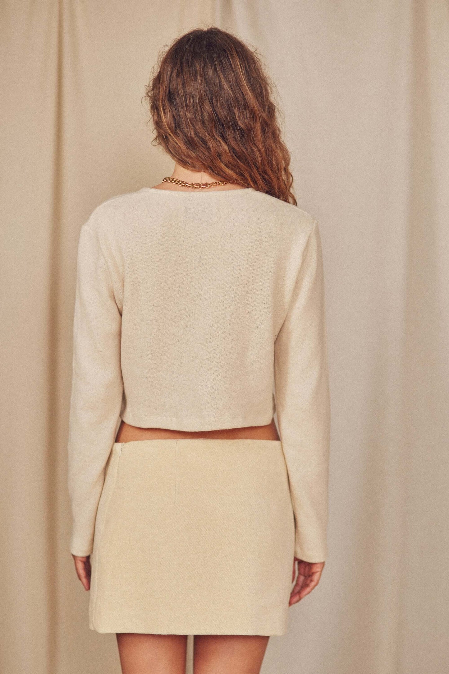 Back view of a model wearing a beige crop top and organic cotton mini skirt with chic thigh split.