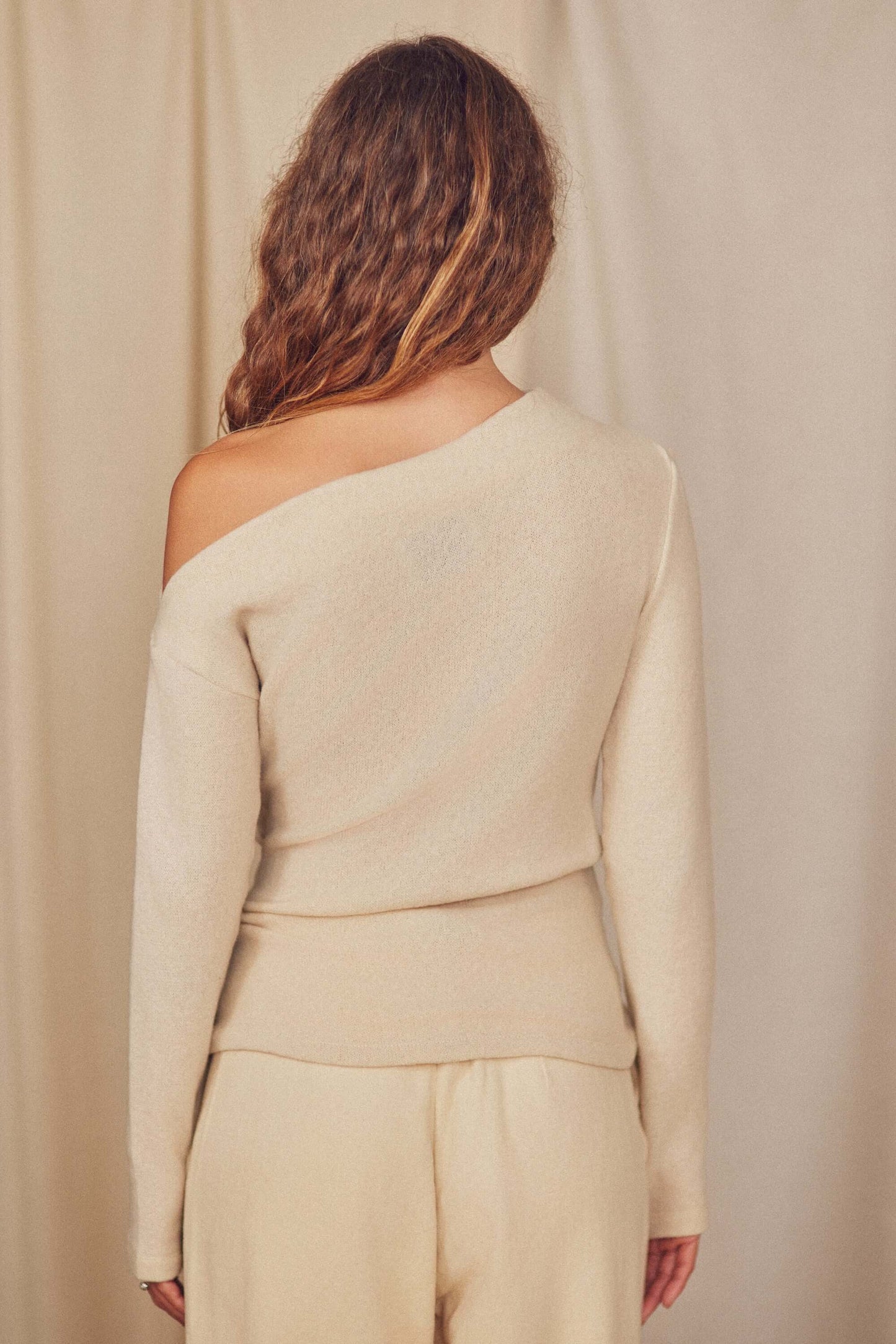Back view of a model wearing an oat wool Fine Knit Drape Top with an off-shoulder design.
