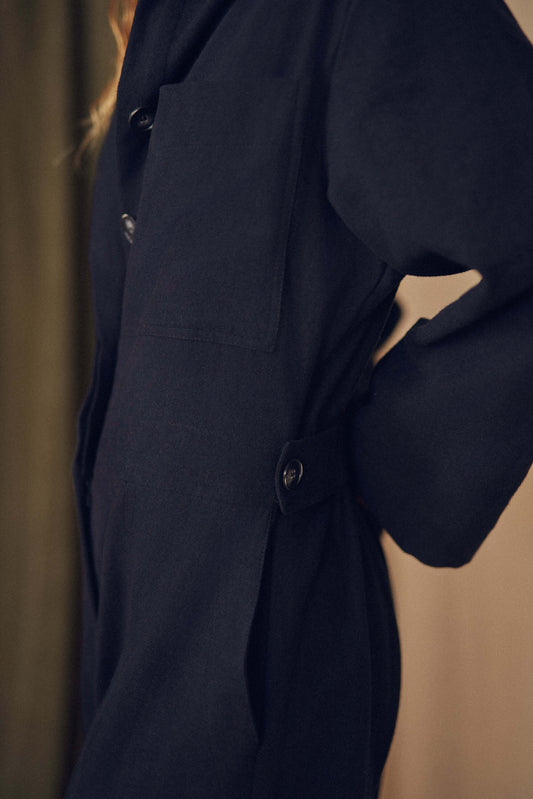 Person wearing a black jumpsuit standing against a beige curtain. Person wearing a black jumpsuit standing against a beige curtain.