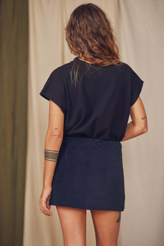 Back view of a model wearing a basic organic cotton black tee with cap sleeves and a dark skirt.