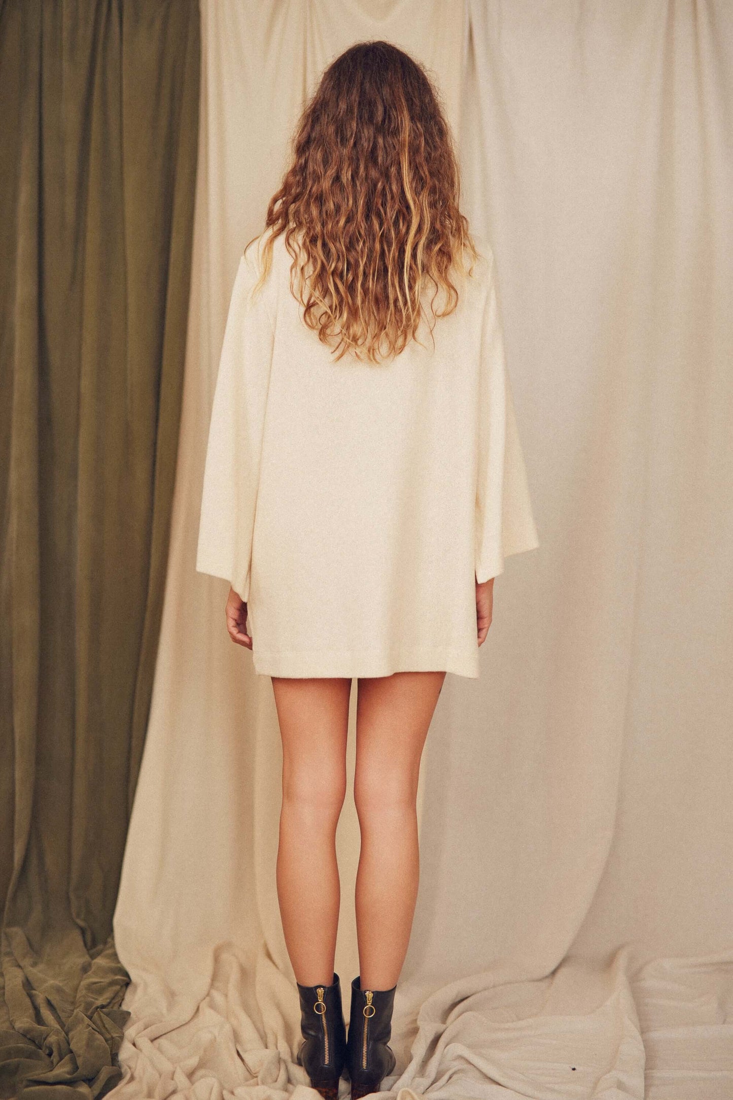 Back view of a model wearing an Oat Fine Knit Mini Dress with flared sleeves, perfect for autumn layering.