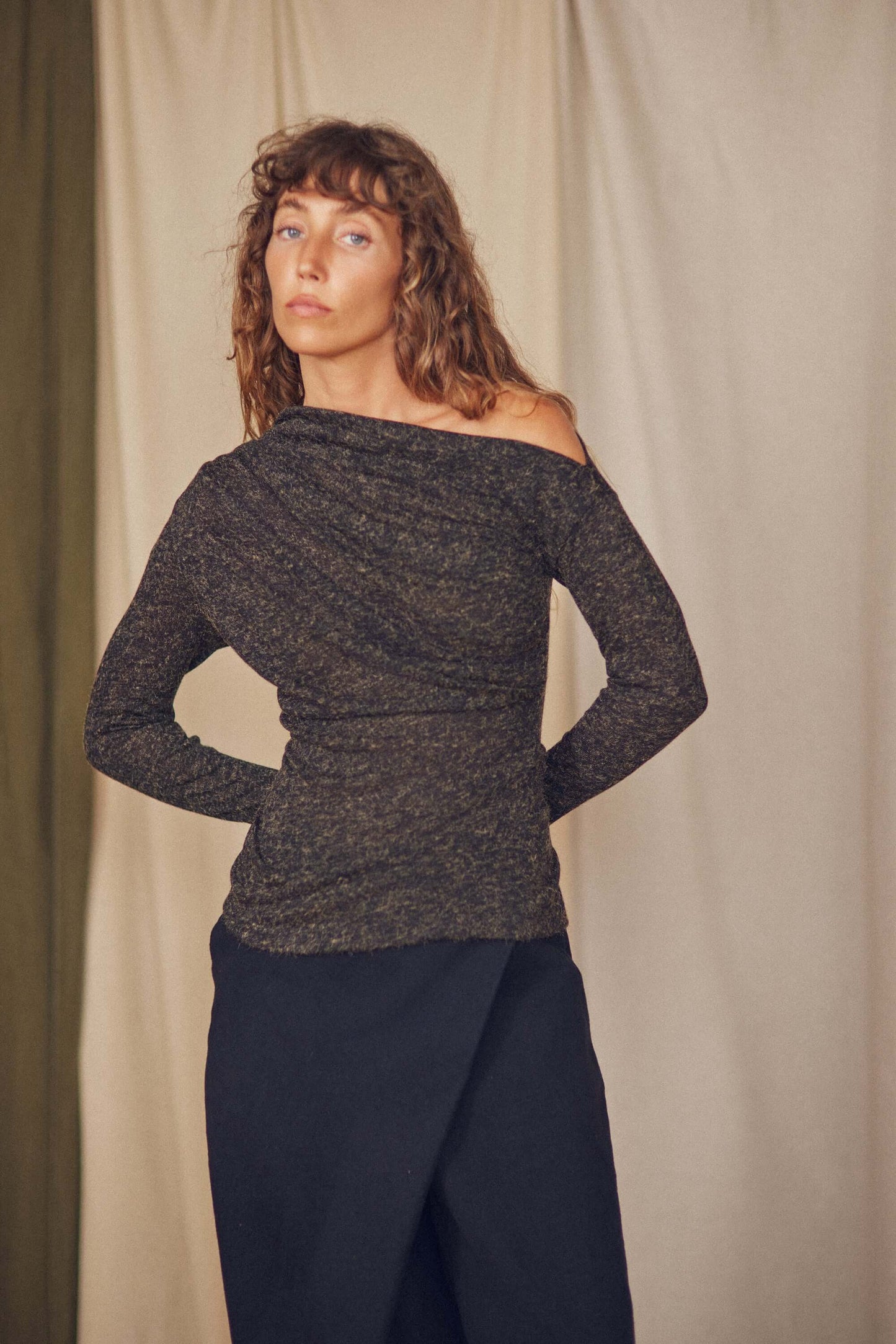 Model wearing a black recycled jersey drape top with a chic neckline and thumb holes, styled with a flowy skirt.