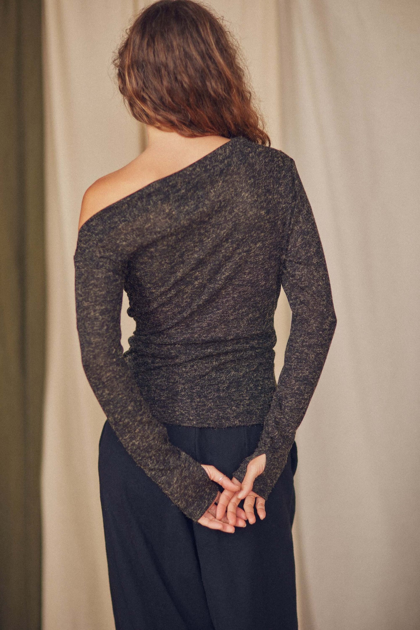 Back view of a woman wearing a chic black recycled jersey drape top with long sleeves and thumb holes.