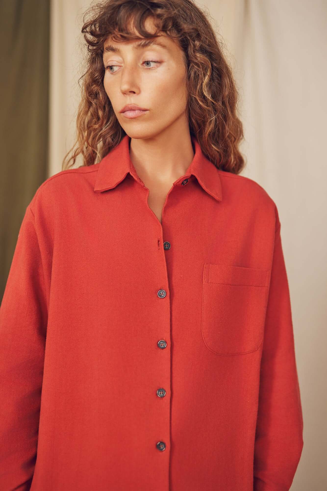 Model wearing a warm rust organic cotton wide overshirt, featuring a pocket and eco-friendly buttons.