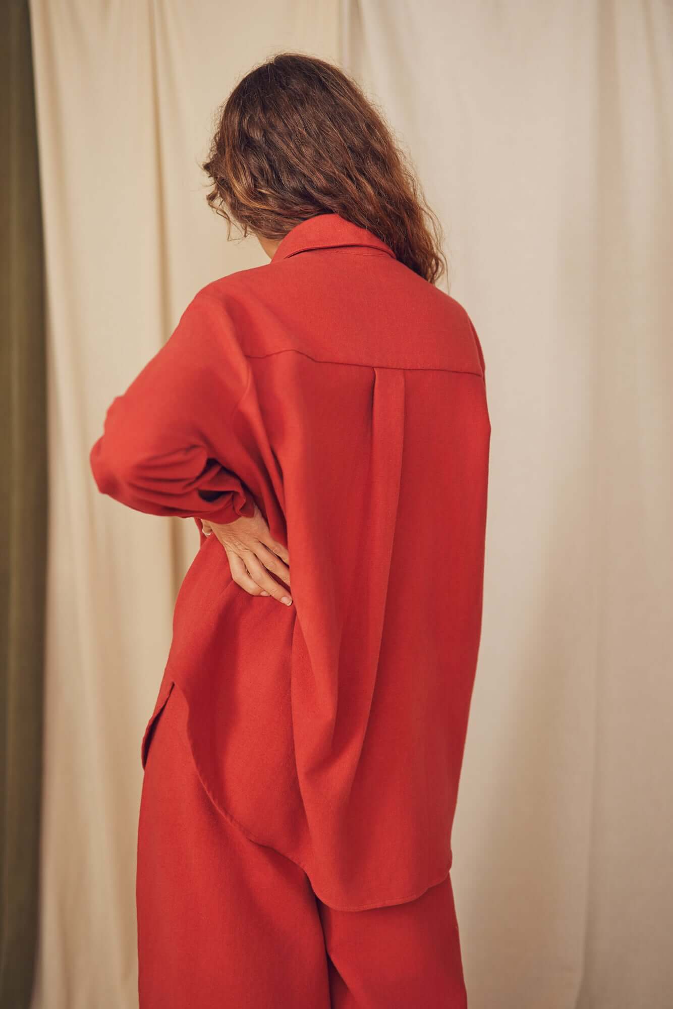 Model wearing a rust organic cotton wide overshirt, showcasing the back design and oversized fit against a soft backdrop.