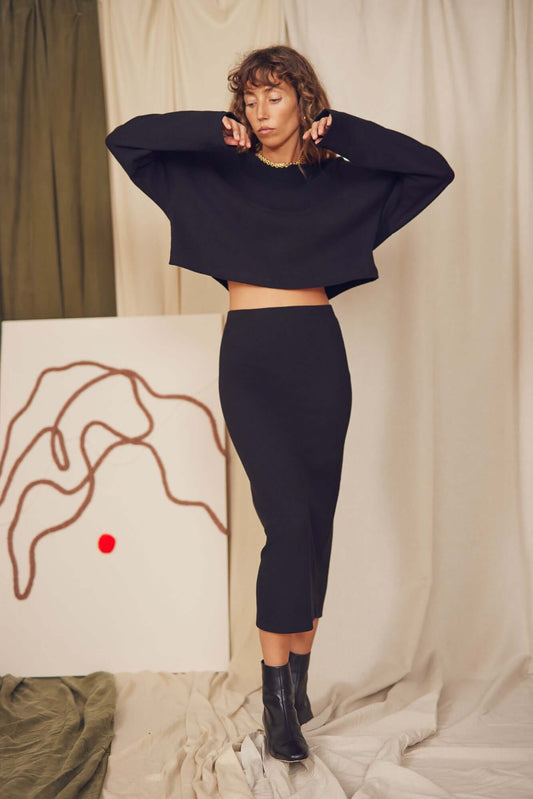Model wearing a black organic cotton midi pencil skirt with a matching cropped sweater, styled for autumn.