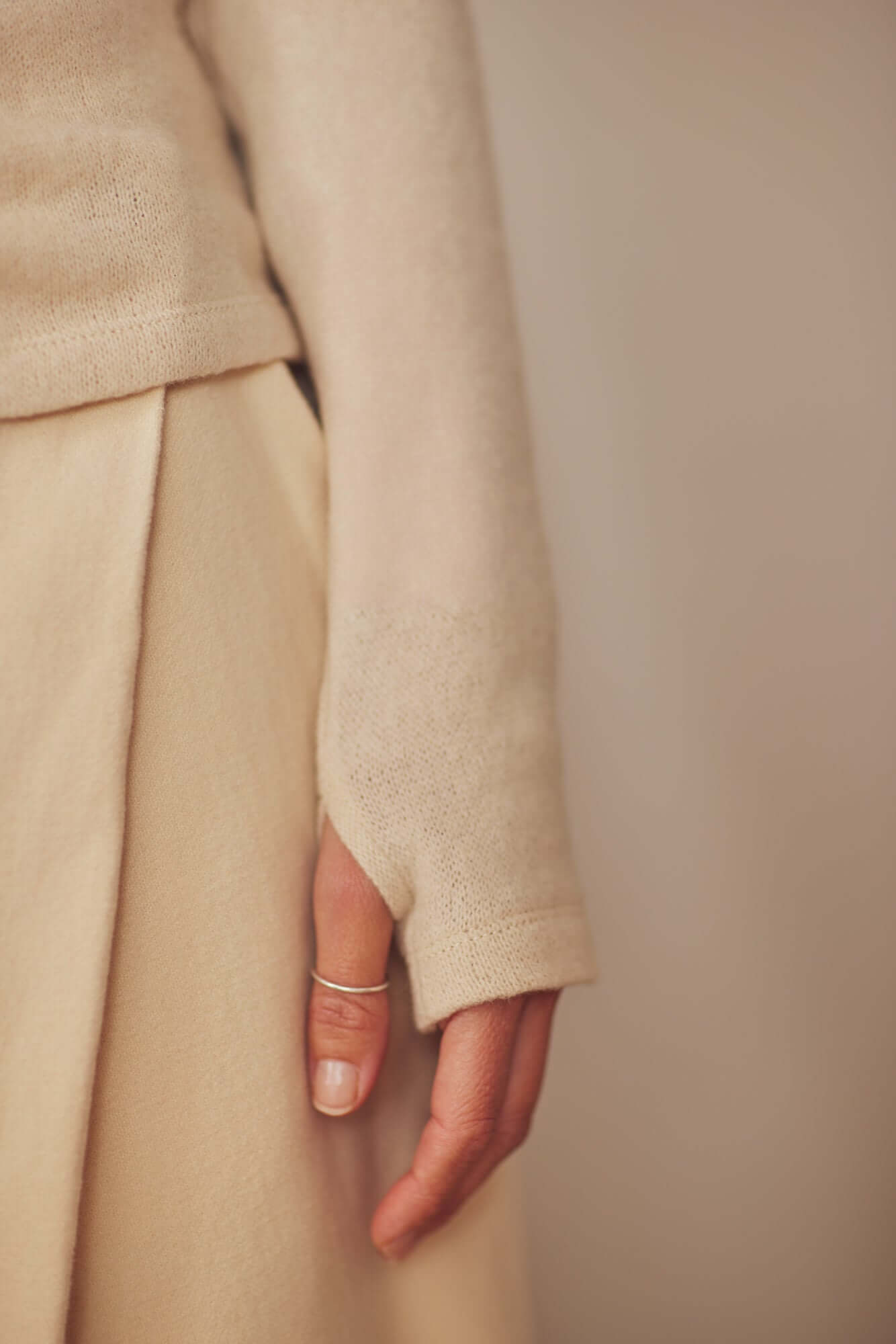 Close-up of a hand wearing the Oat Wool Fine Knit Drape Top with thumb holes, showcasing modern and functional design.