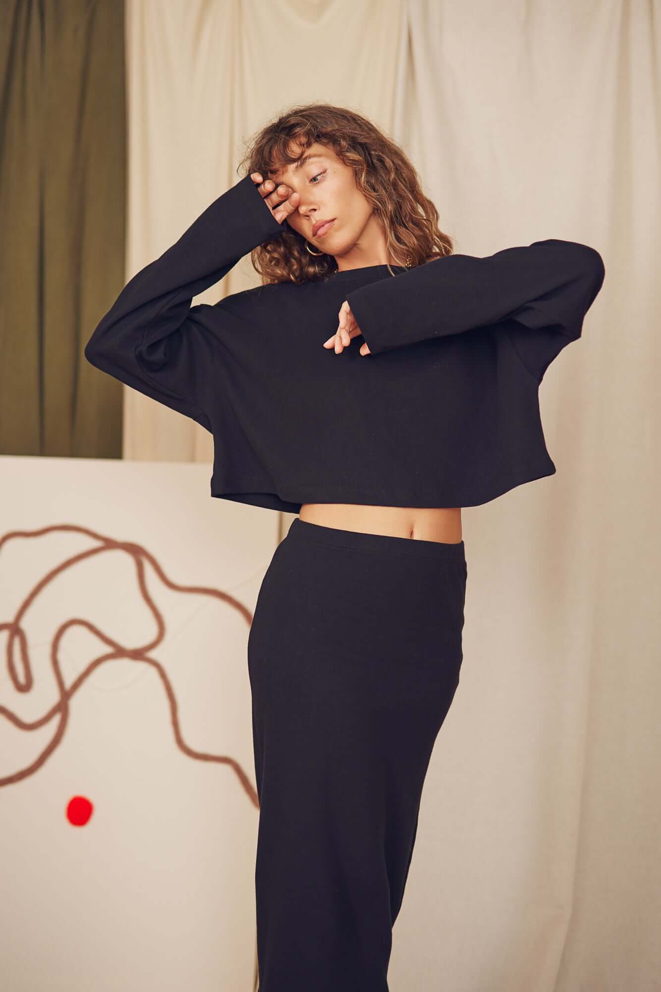 Model wearing a black organic cotton midi skirt with a cropped black top, showcasing minimalist autumn style.