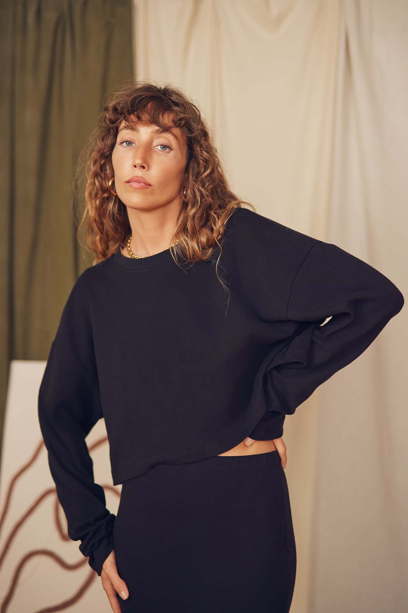 Model wearing a black organic cotton long sleeve crop top, styled for autumn/winter layering.