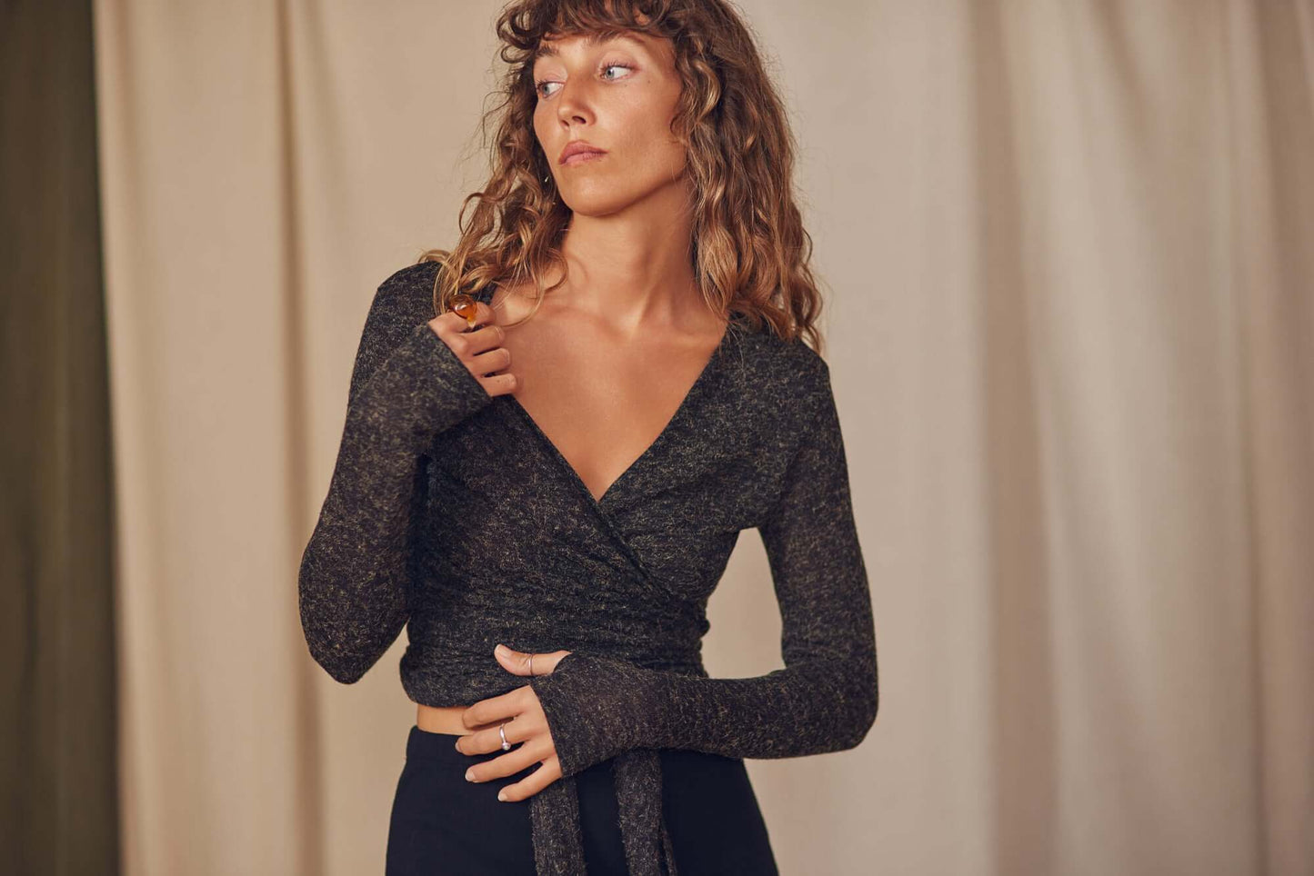 Woman wearing a black multiway recycled jersey wrap top with long sleeves and thumb holes, styled for autumn/winter.