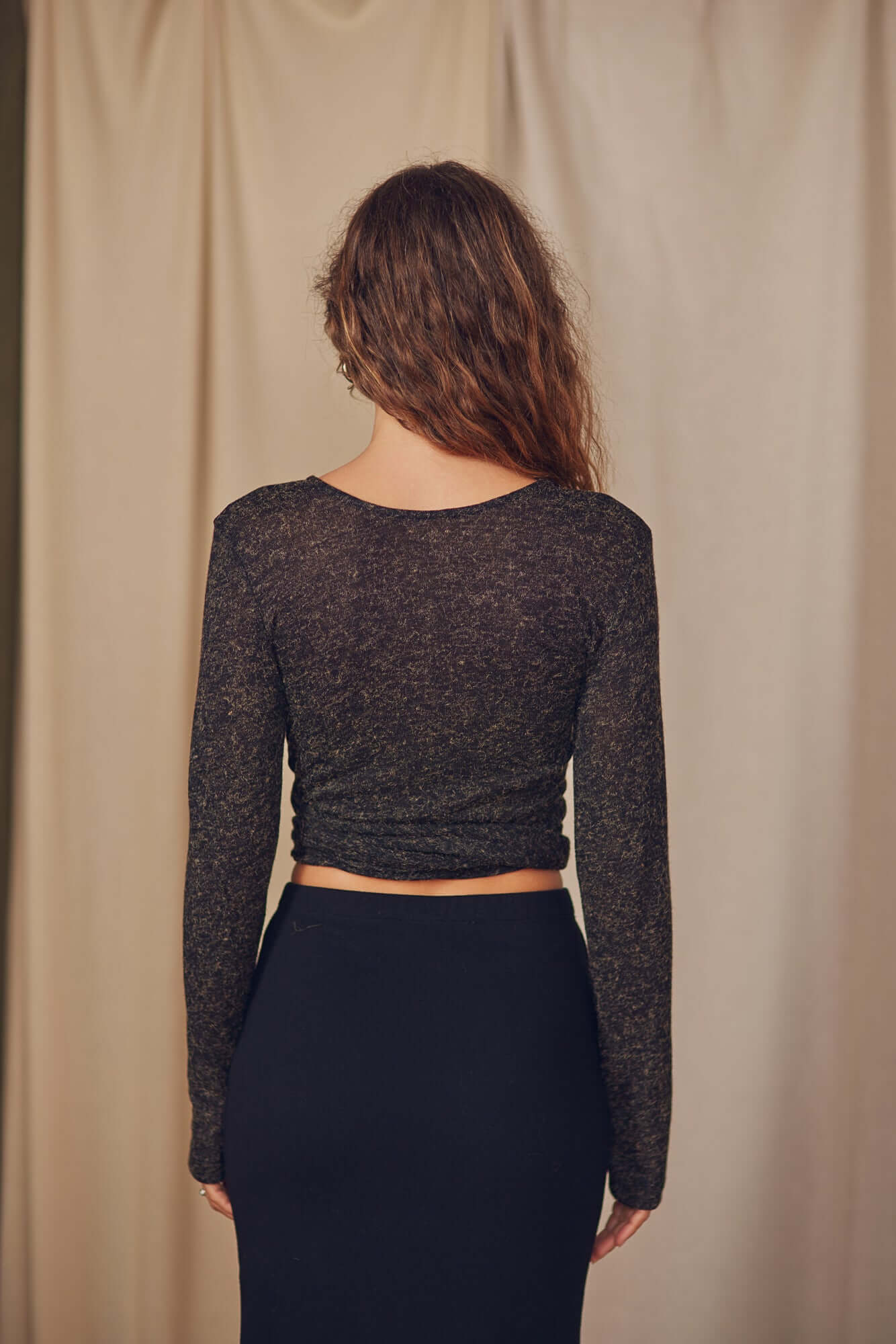 Back view of a woman wearing a black multiway recycled jersey wrap top paired with a black skirt.