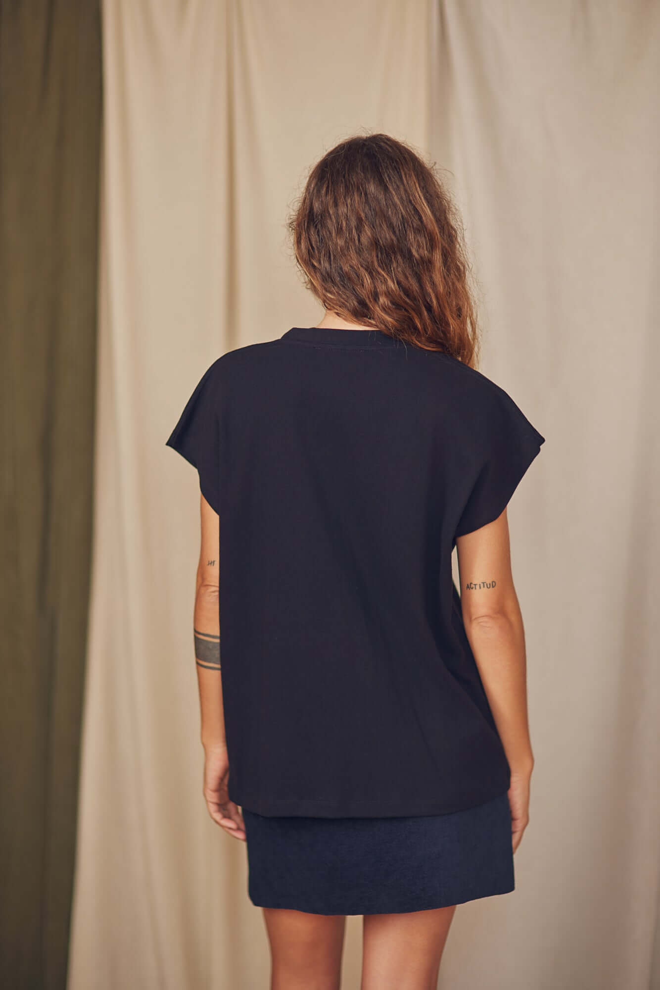Back view of a woman wearing a black organic cotton tee with short cap sleeves, styled for autumn/winter.