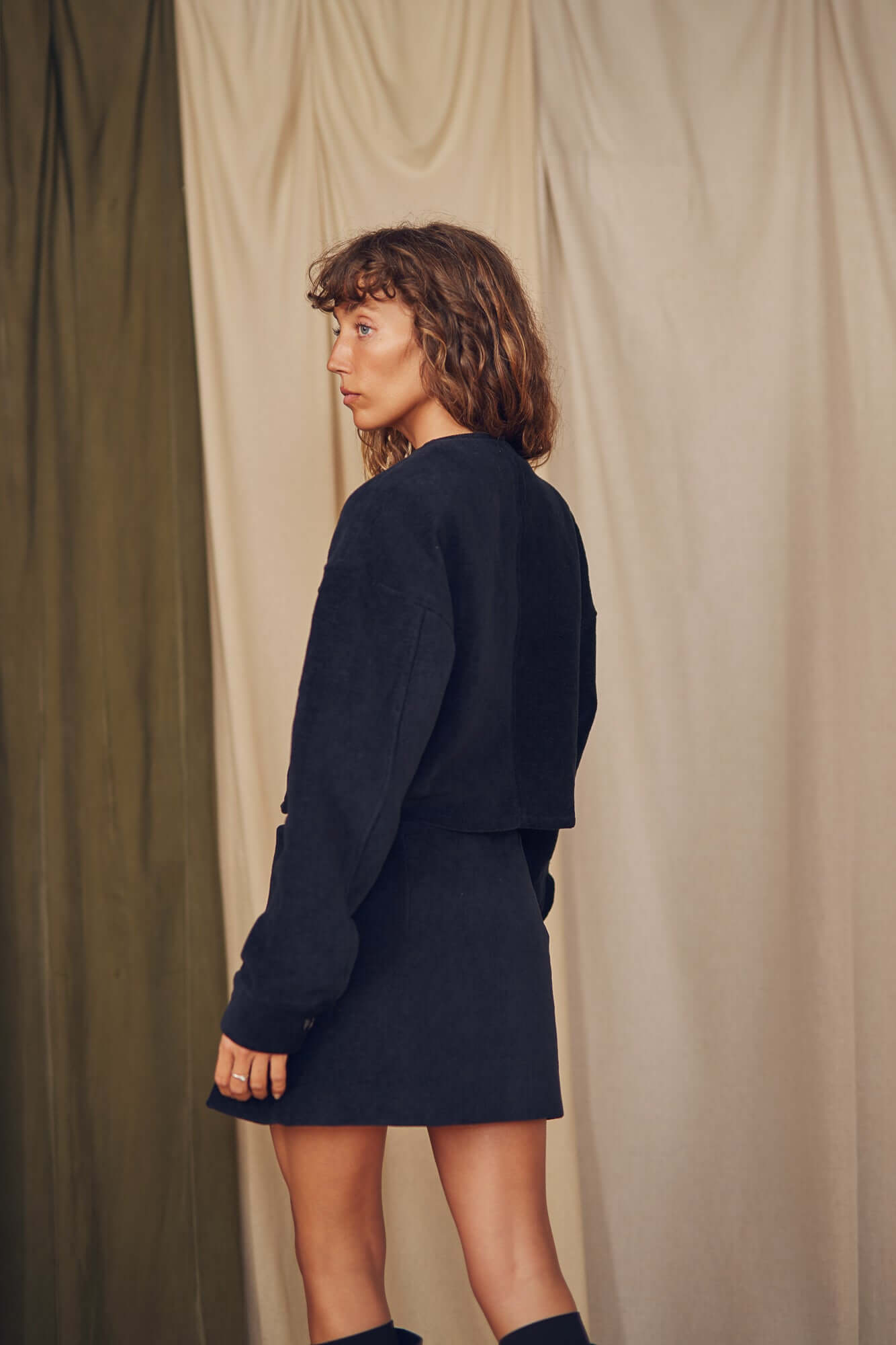 Model wearing a black organic cotton crop jacket, styled with a matching skirt against a neutral backdrop.