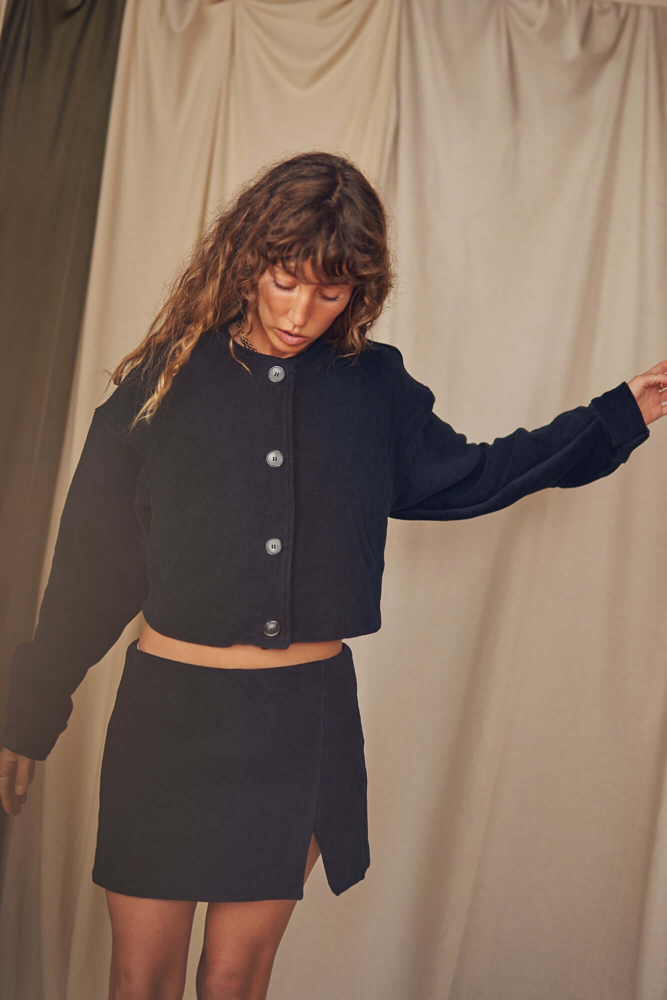 Woman wearing a black organic cotton crop jacket styled with a matching skirt, showcasing sustainable fashion in autumn.