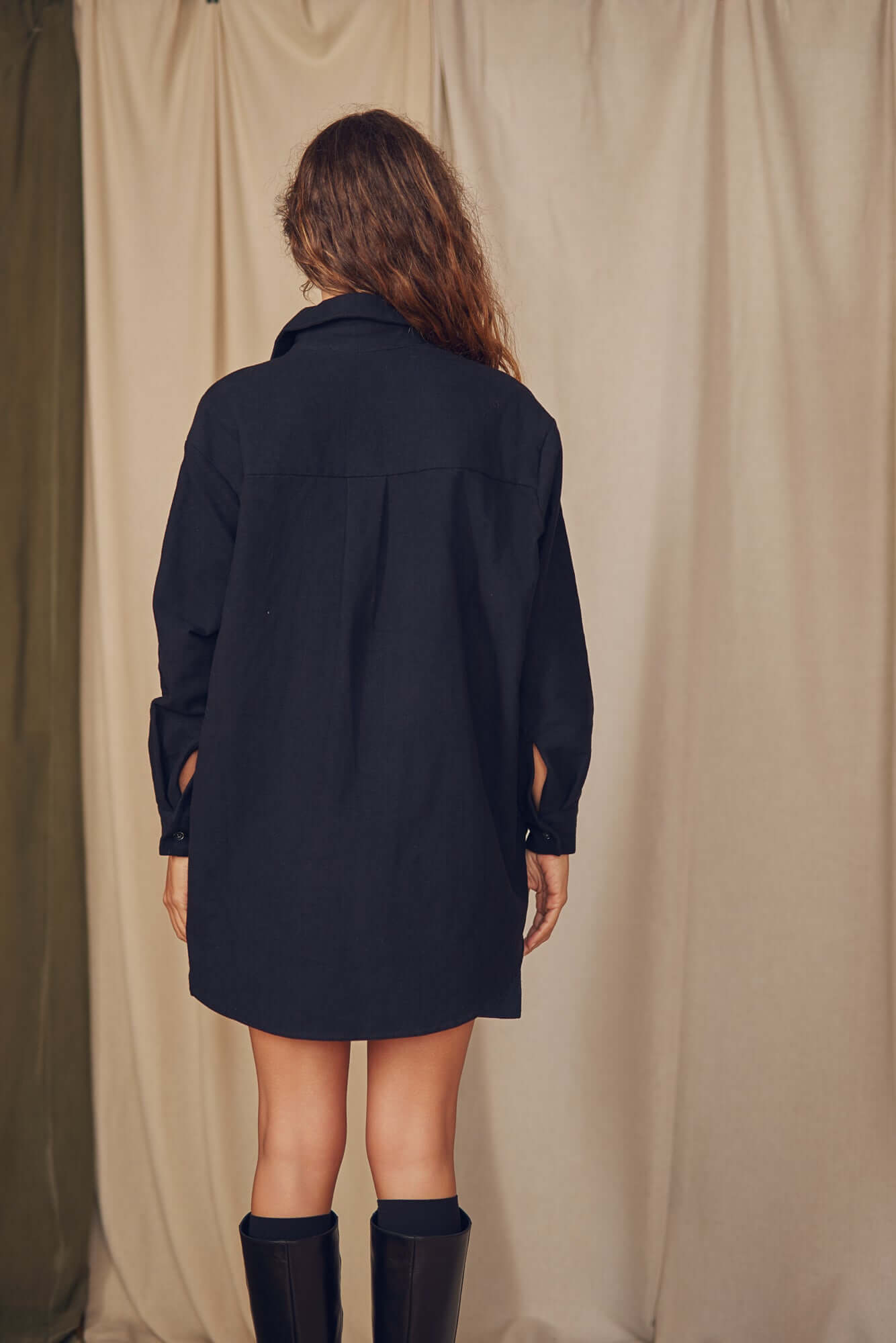 Back view of a model wearing a black organic cotton wide overshirt, showcasing its oversized silhouette.