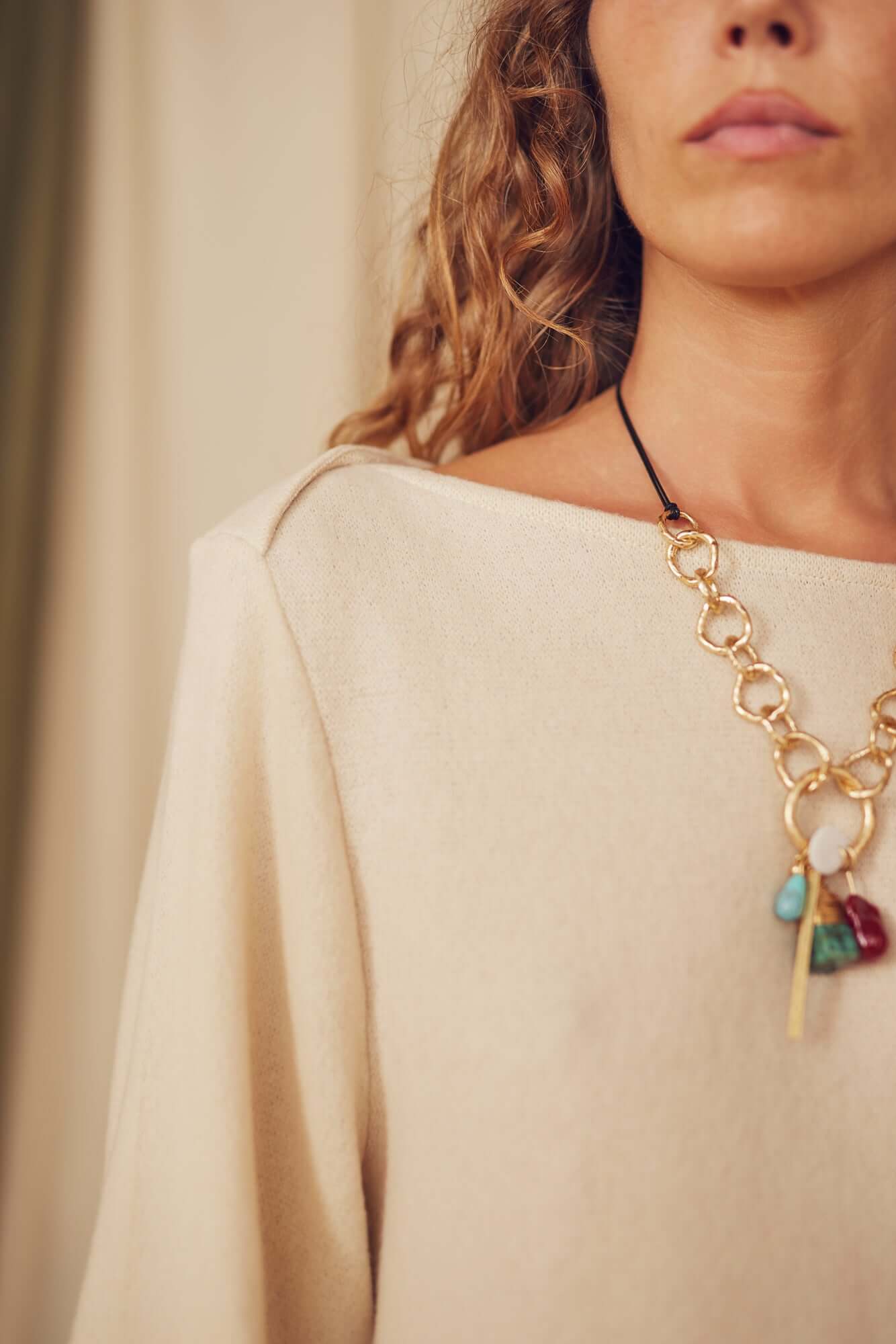 Close-up of a woman wearing a necklace with colored stones, showcasing an oat fine knit mini dress.