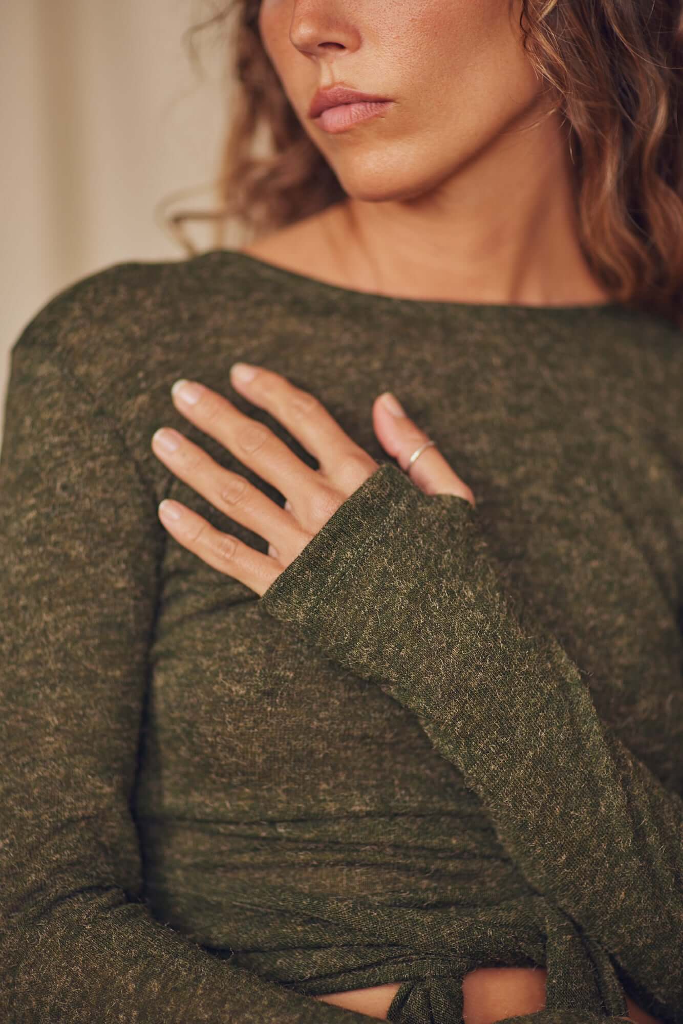 Close-up of a woman wearing a khaki recycled jersey wrap top with long sleeves and thumb holes.