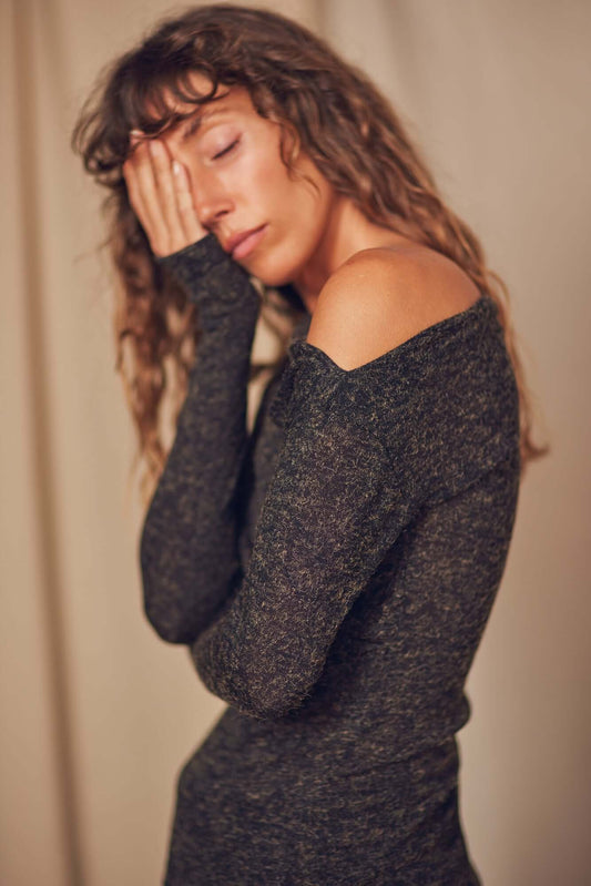Woman wearing a black recycled jersey dress with draped neckline, showing a relaxed pose against a soft background.